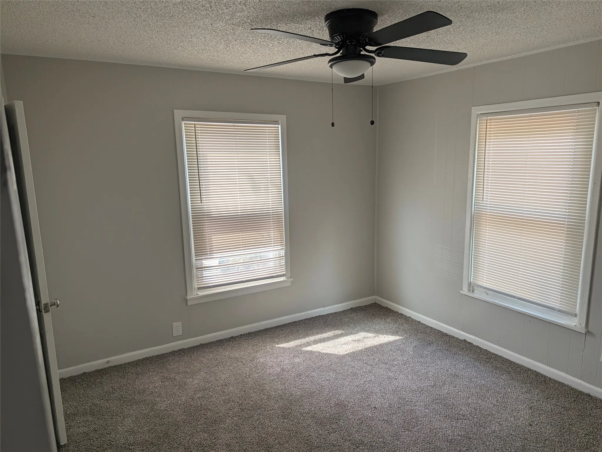 Neutral-toned walls, ceiling fan with integrated lighting, two windows with blinds, and gray carpeting