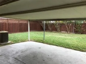 Covered concrete patio with a spacious grass lawn and a wood privacy fence