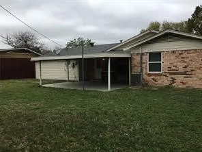 Expansive grassy area with a brick exterior, covered patio, and a separate storage structure