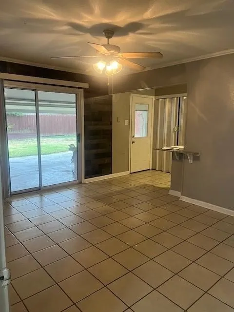 Tiled flooring, ceiling fan with integrated lighting, sliding glass door, white paneled interior door, and a built-in wall shelf