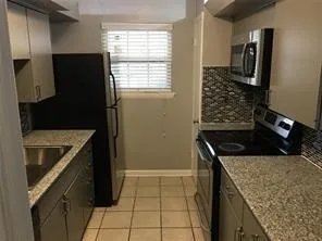 Kitchen featuring ceramic tile flooring, stainless steel sink, light-toned cabinetry, and granite-style countertops