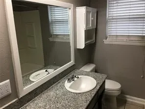 Granite-finish countertop with an integrated sink, framed wall mirror, built-in wall cabinet, and a window with blinds