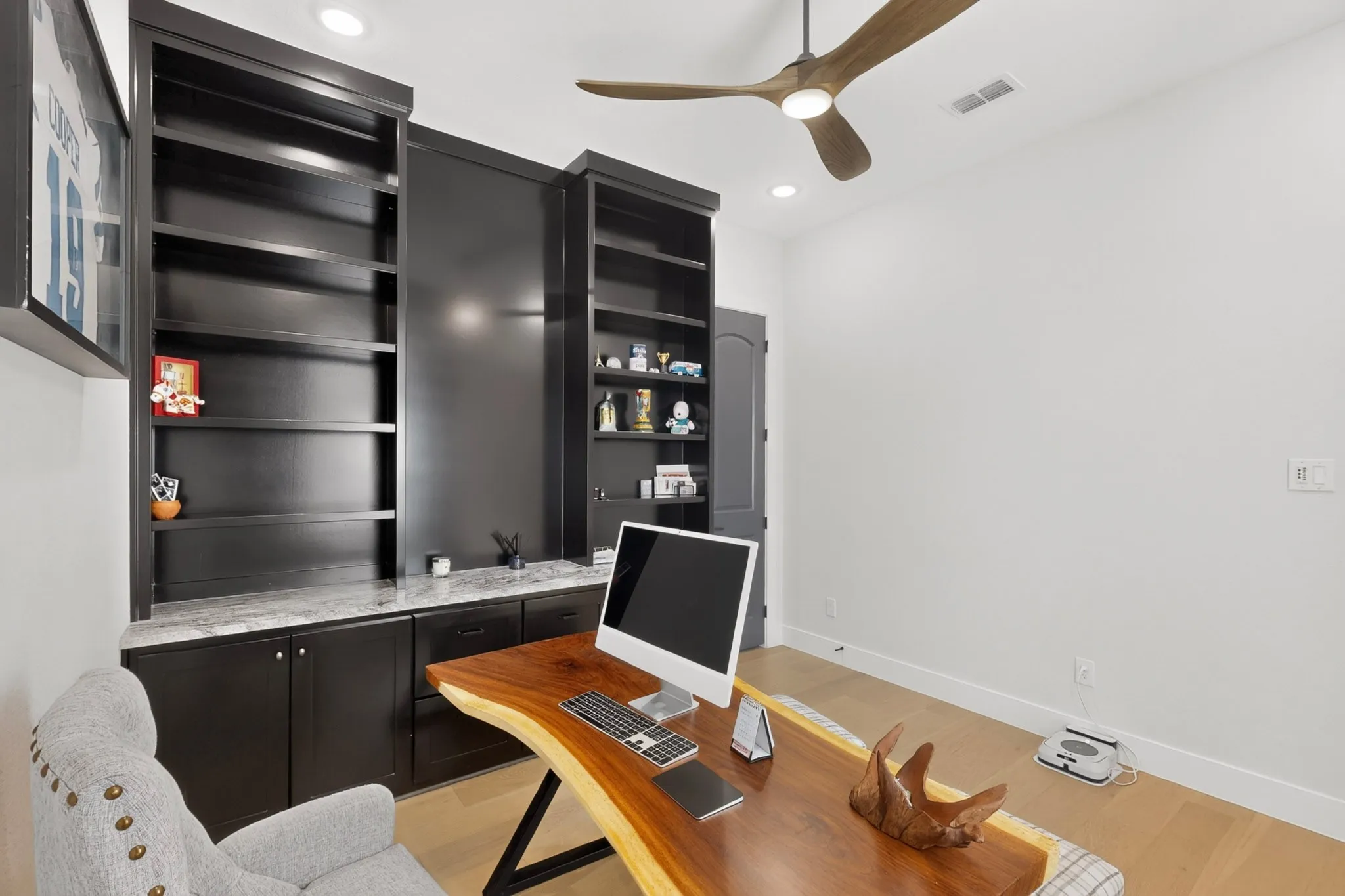 Built-in black cabinetry, integrated shelving, stone-finish countertop, wood-finish flooring, and a ceiling fan with integrated lighting