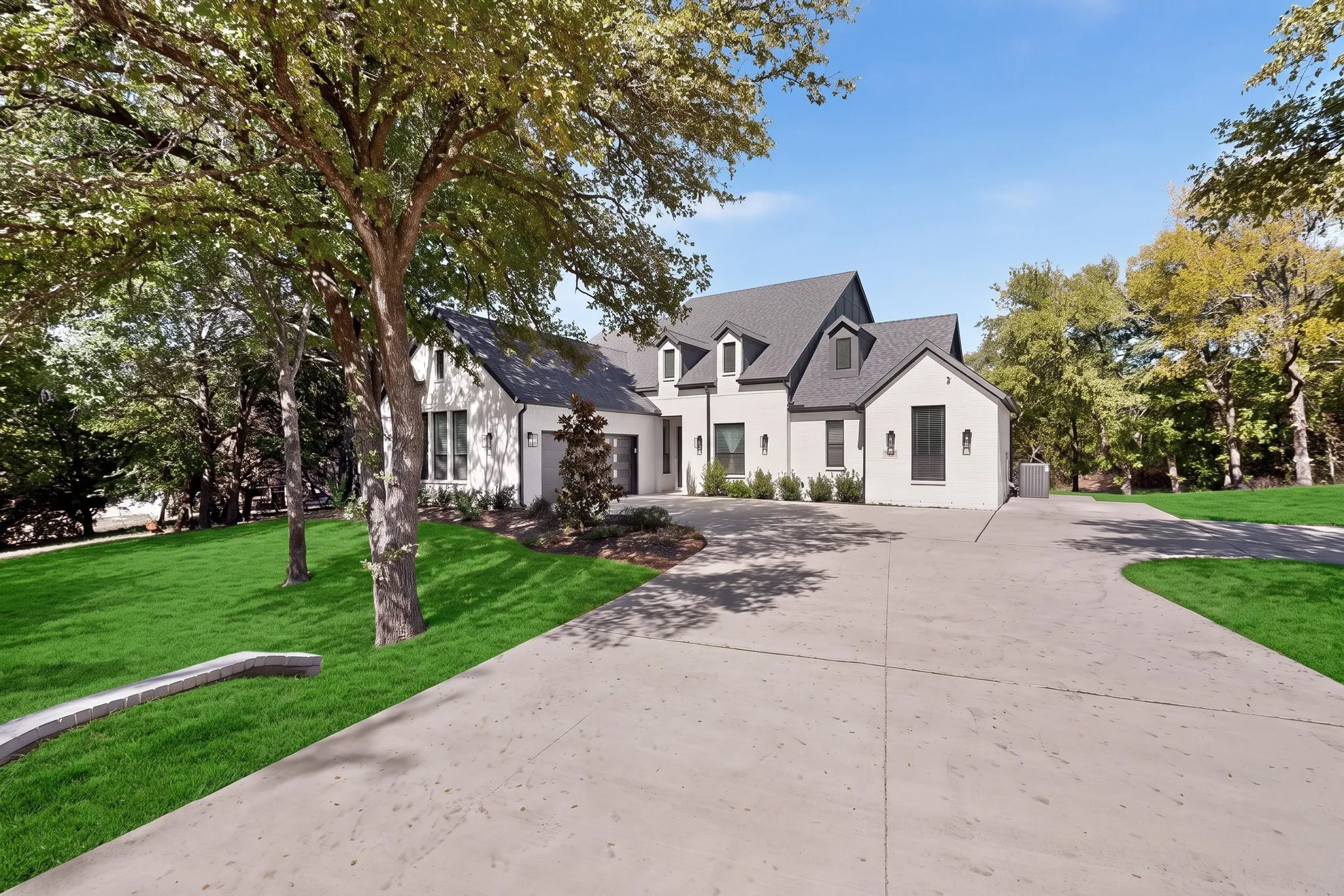White painted brick exterior with dark gray roofing, multiple dormer windows, and a concrete driveway