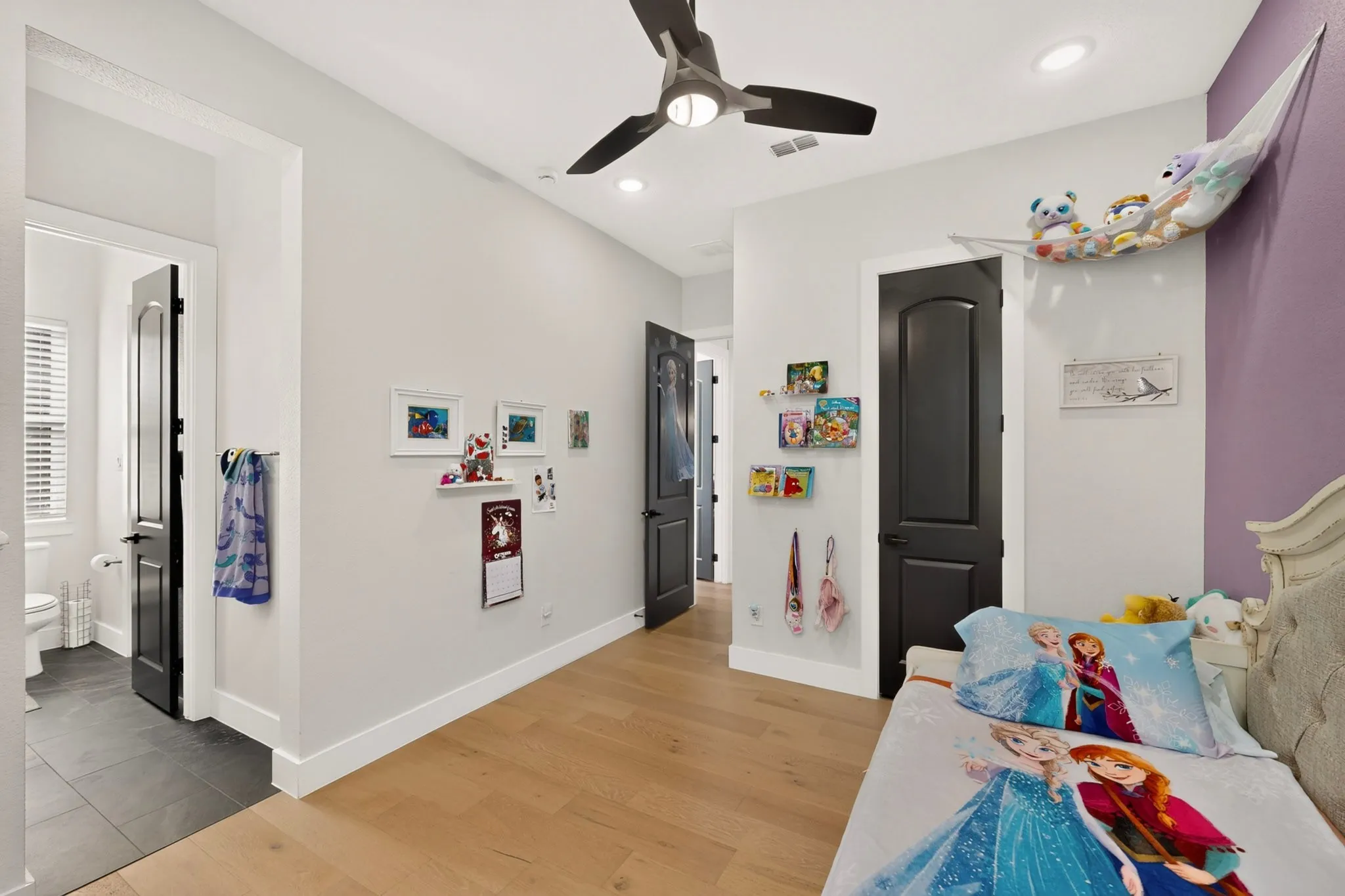 Light wood-finish flooring, recessed ceiling lighting, a ceiling fan, and a solid black interior door