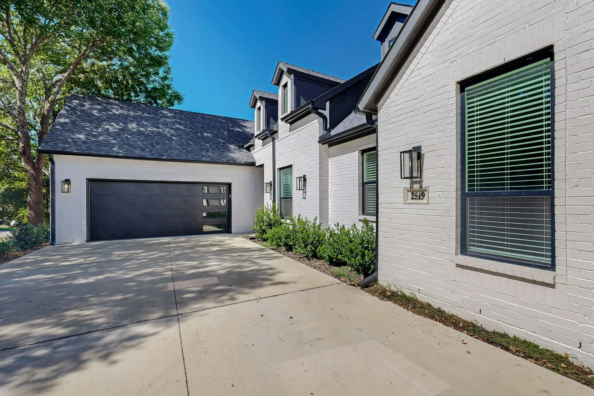 White brick exterior with black framed windows, a black garage door with integrated glass panels, and exterior wall lanterns