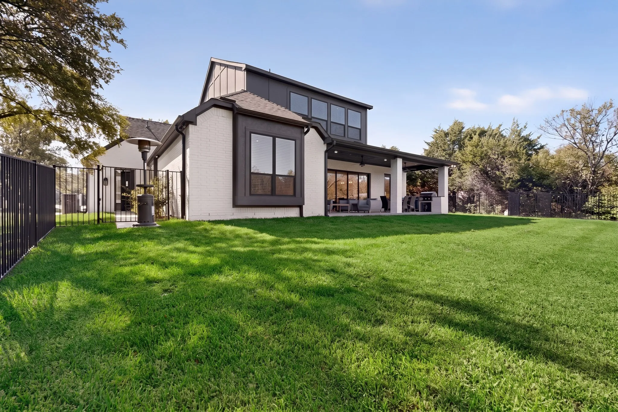 Expansive backyard featuring a manicured lawn, covered patio, and black metal fencing