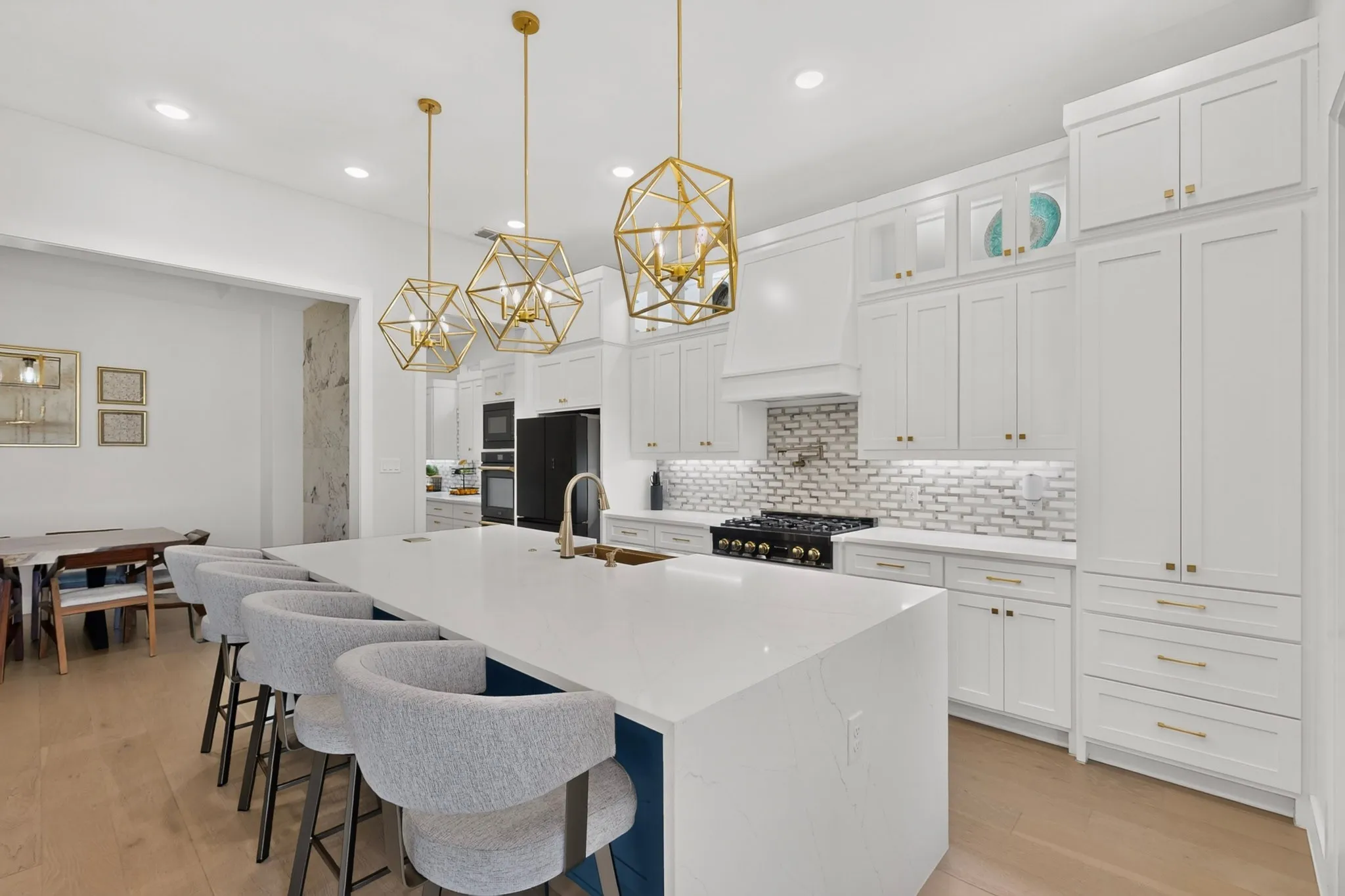 White cabinetry with gold-tone hardware, white subway tile backsplash, stainless steel range with hood, wood-finish flooring, and a large central island with seating