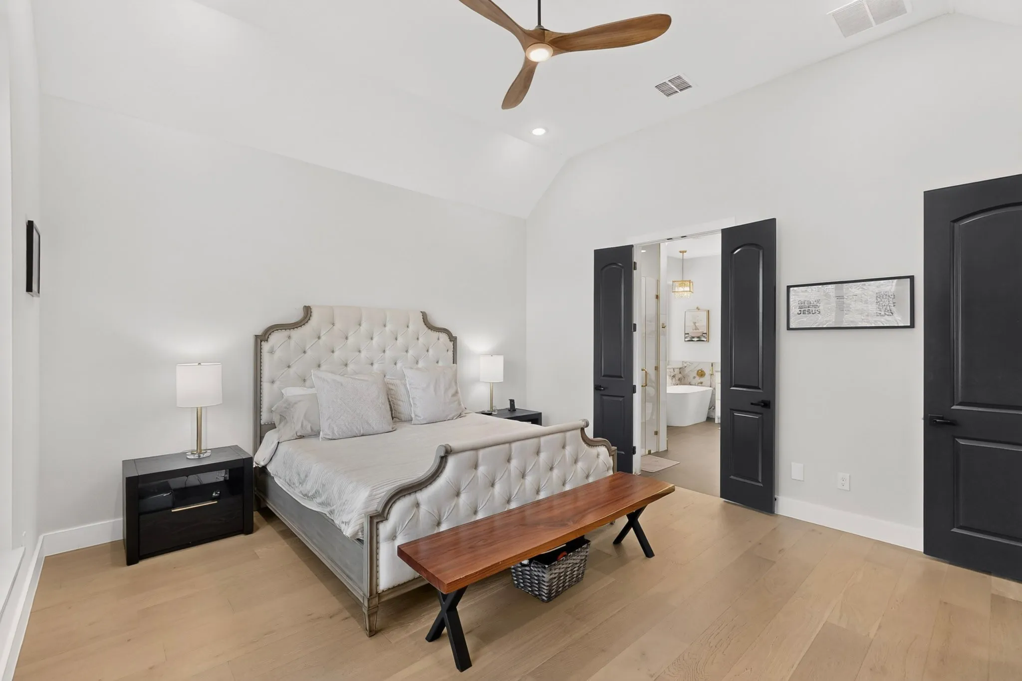 Vaulted ceiling, ceiling fan, natural wood-finish flooring, black interior doors, and a bathroom with a freestanding tub
