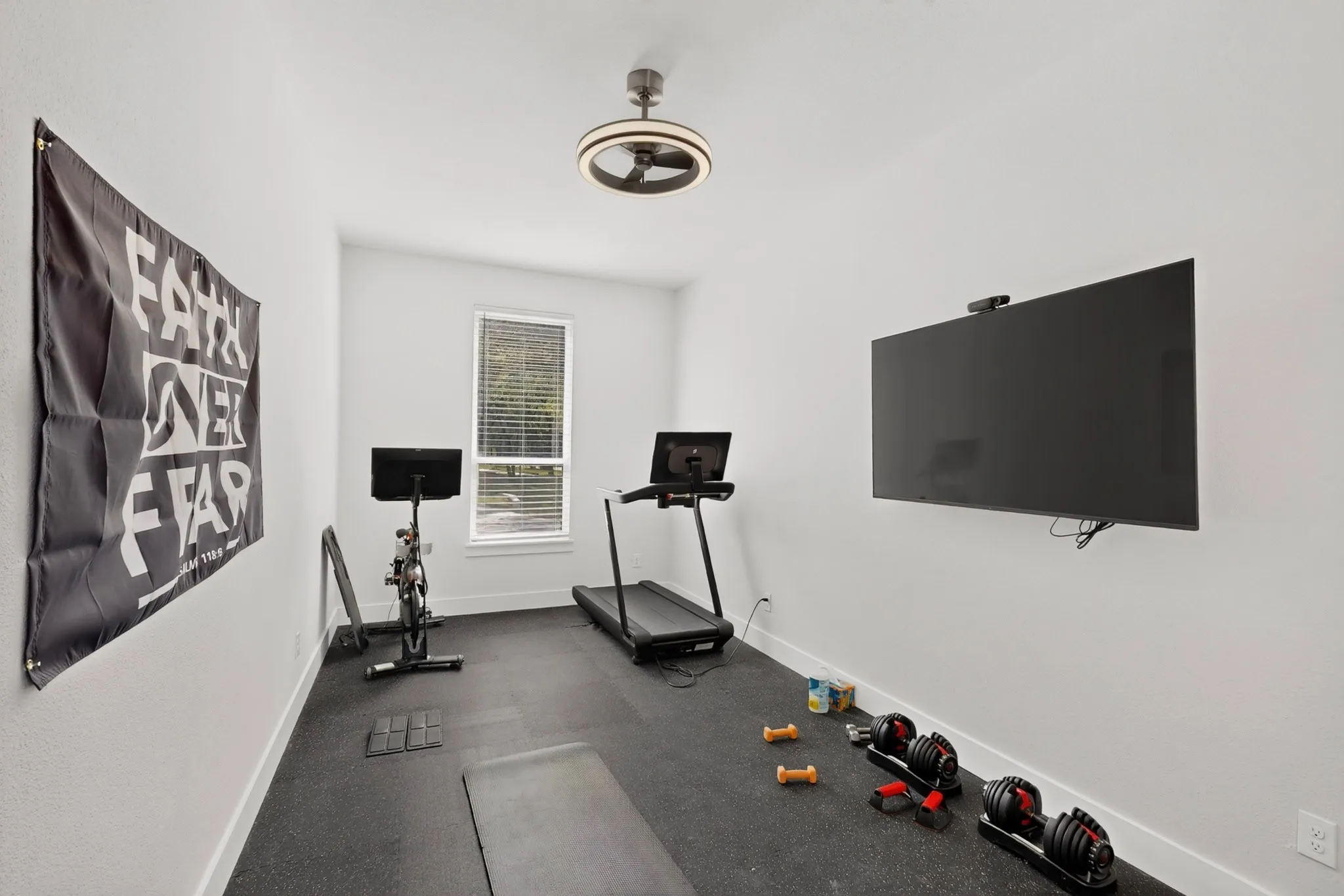 Dedicated fitness space with resilient rubber flooring, a single window with blinds, and a contemporary ceiling light fixture
