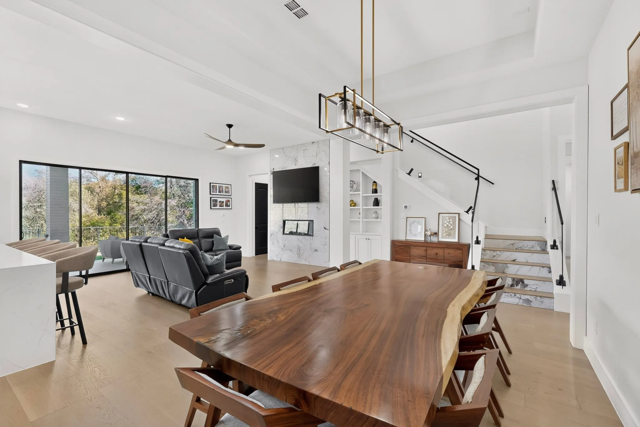 Open-concept living space featuring wood-finish flooring, a contemporary fireplace with a stone surround, and an elegant staircase with a black metal railing