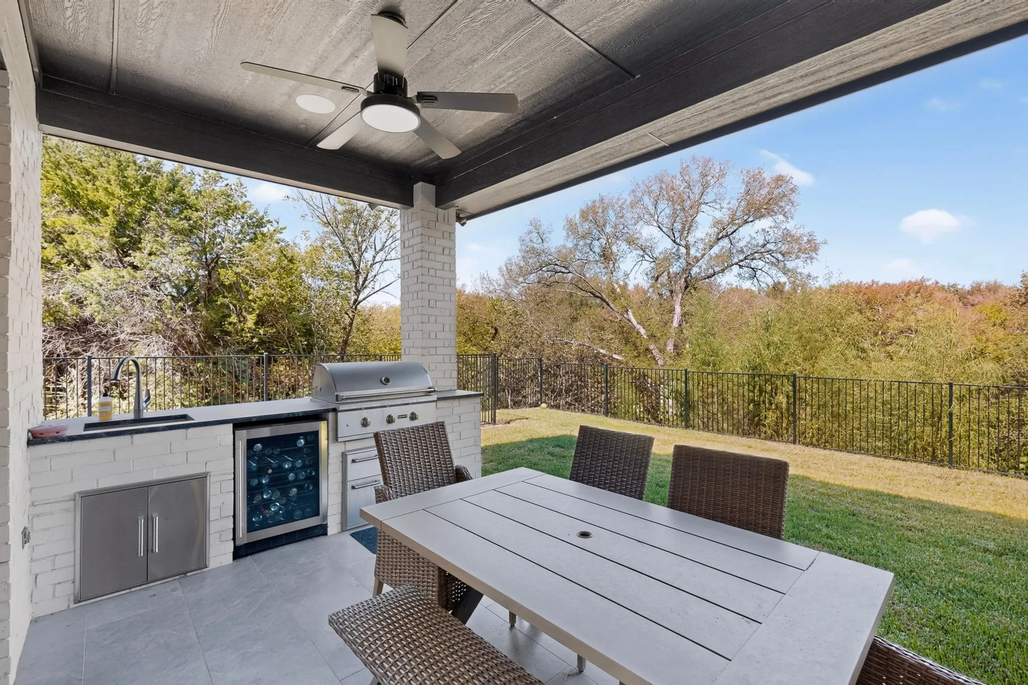Covered patio with a built-in outdoor kitchen, stainless steel grill, refrigerator, and sink, set on a tiled surface