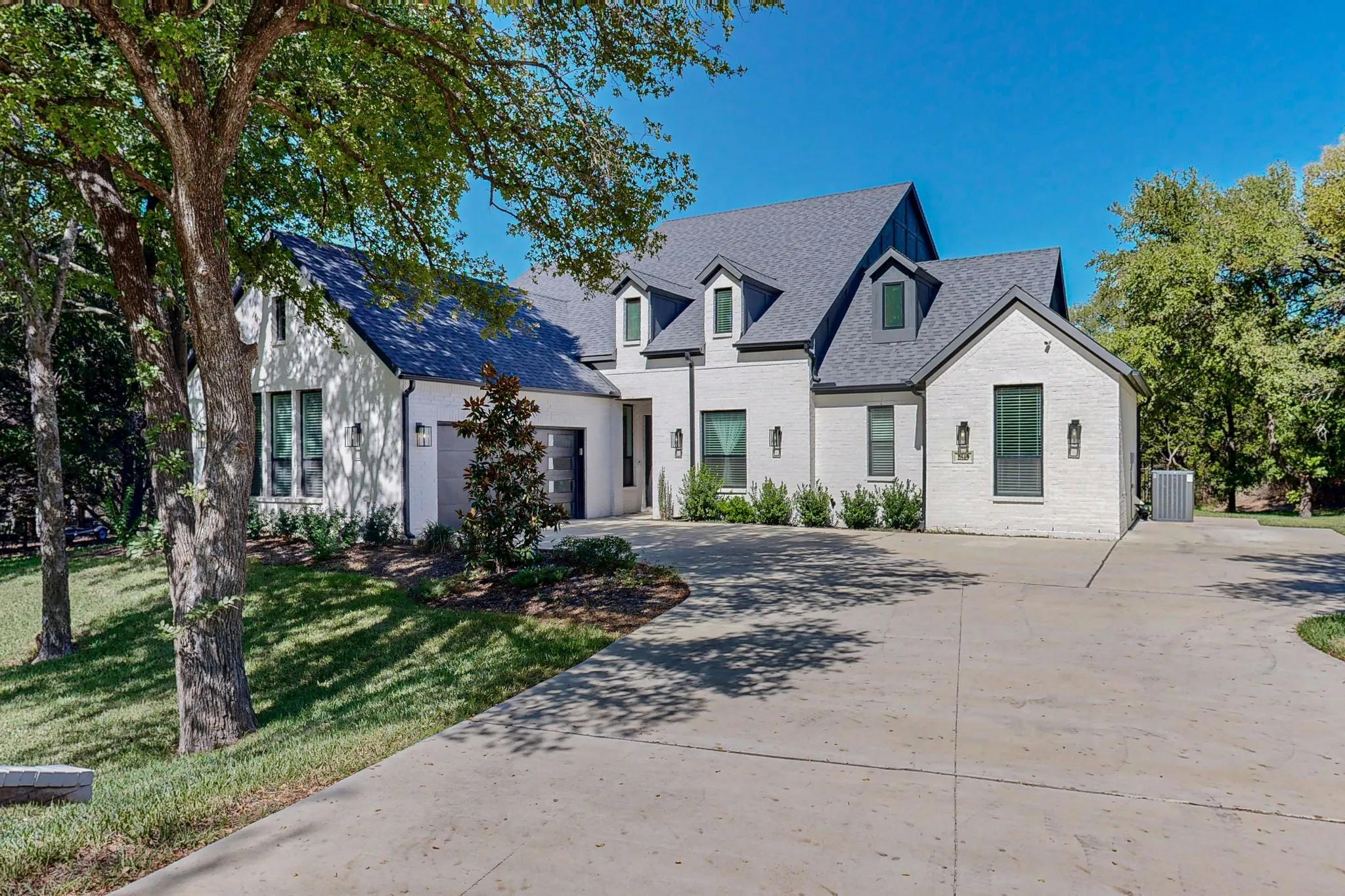 White brick exterior with dark trim windows, multi-pitch roofline, dormer windows, and a concrete driveway