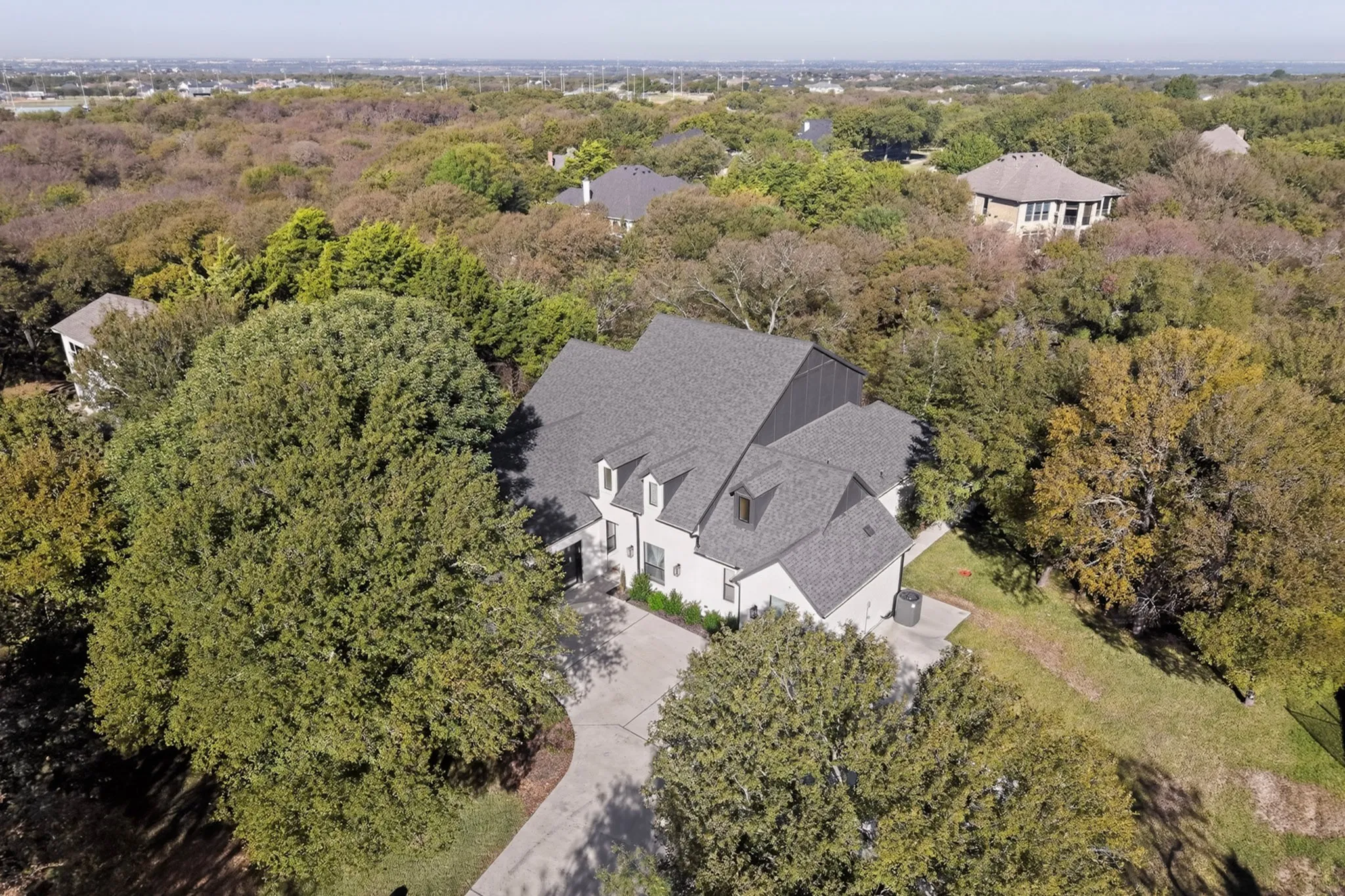 Multi-story residence featuring a gray shingle roof and dormer windows, surrounded by mature trees