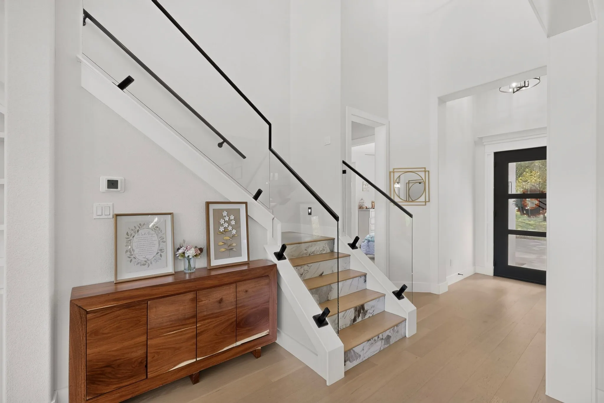 Contemporary staircase with glass panel railing and black handrail, light wood-finish flooring, and white walls
