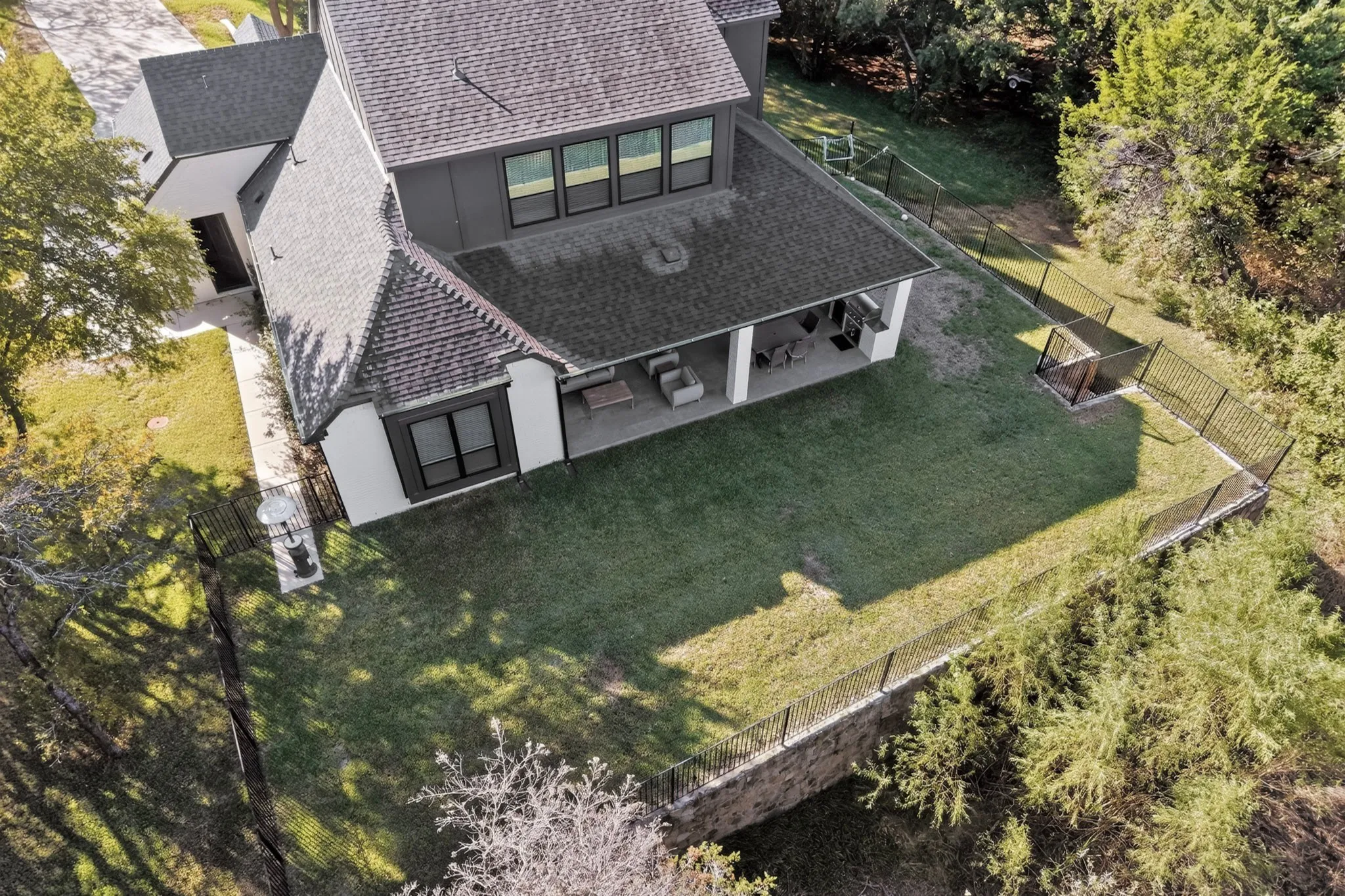 Two-story exterior with a covered patio, a manicured lawn, and a black wrought iron fence
