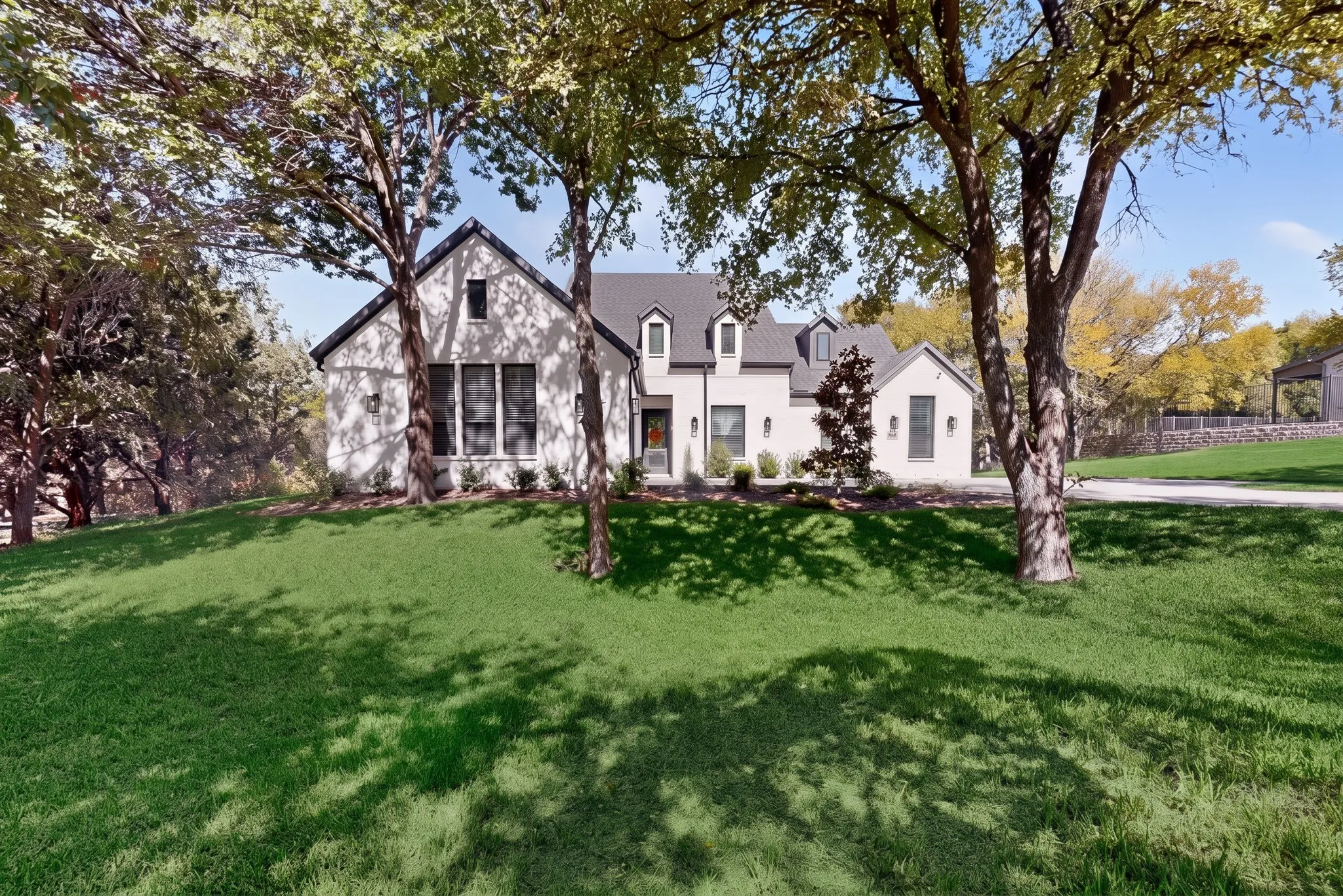 White exterior with dark trim accents, dormer windows, a covered entry, established trees, and a concrete driveway