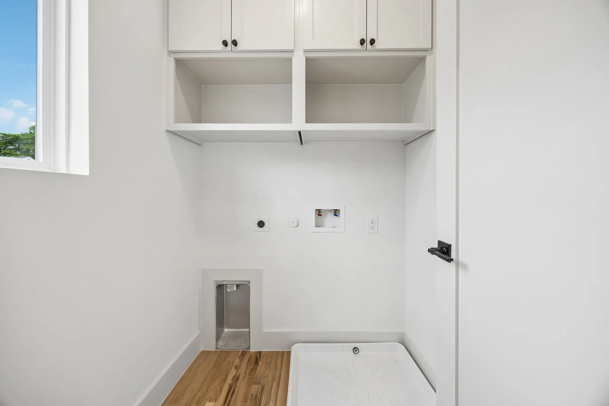 White shaker cabinetry with black hardware, wood-finish flooring, and a white window frame