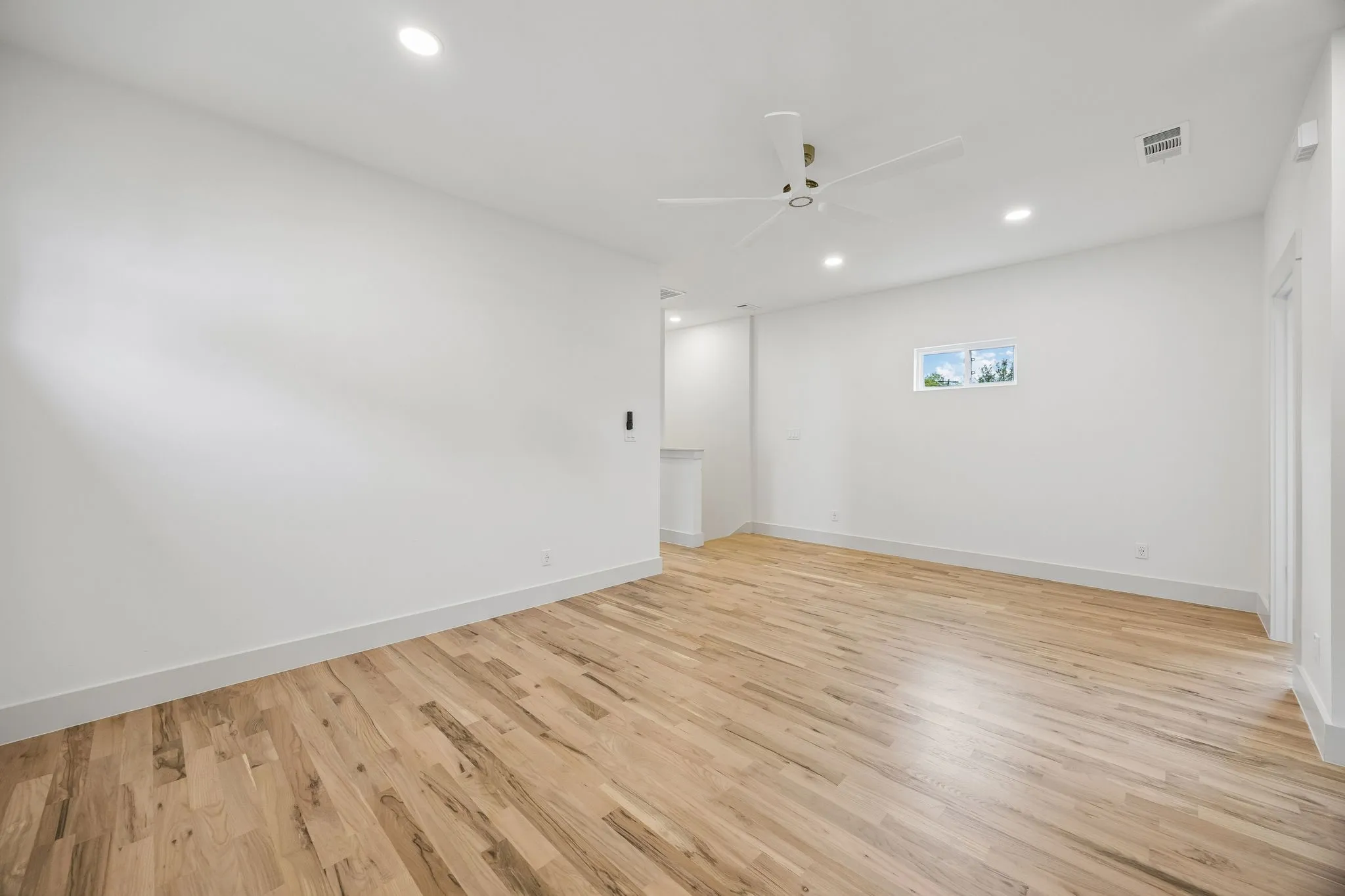 Recessed lighting and a ceiling fan illuminate a spacious room with wood-finish flooring