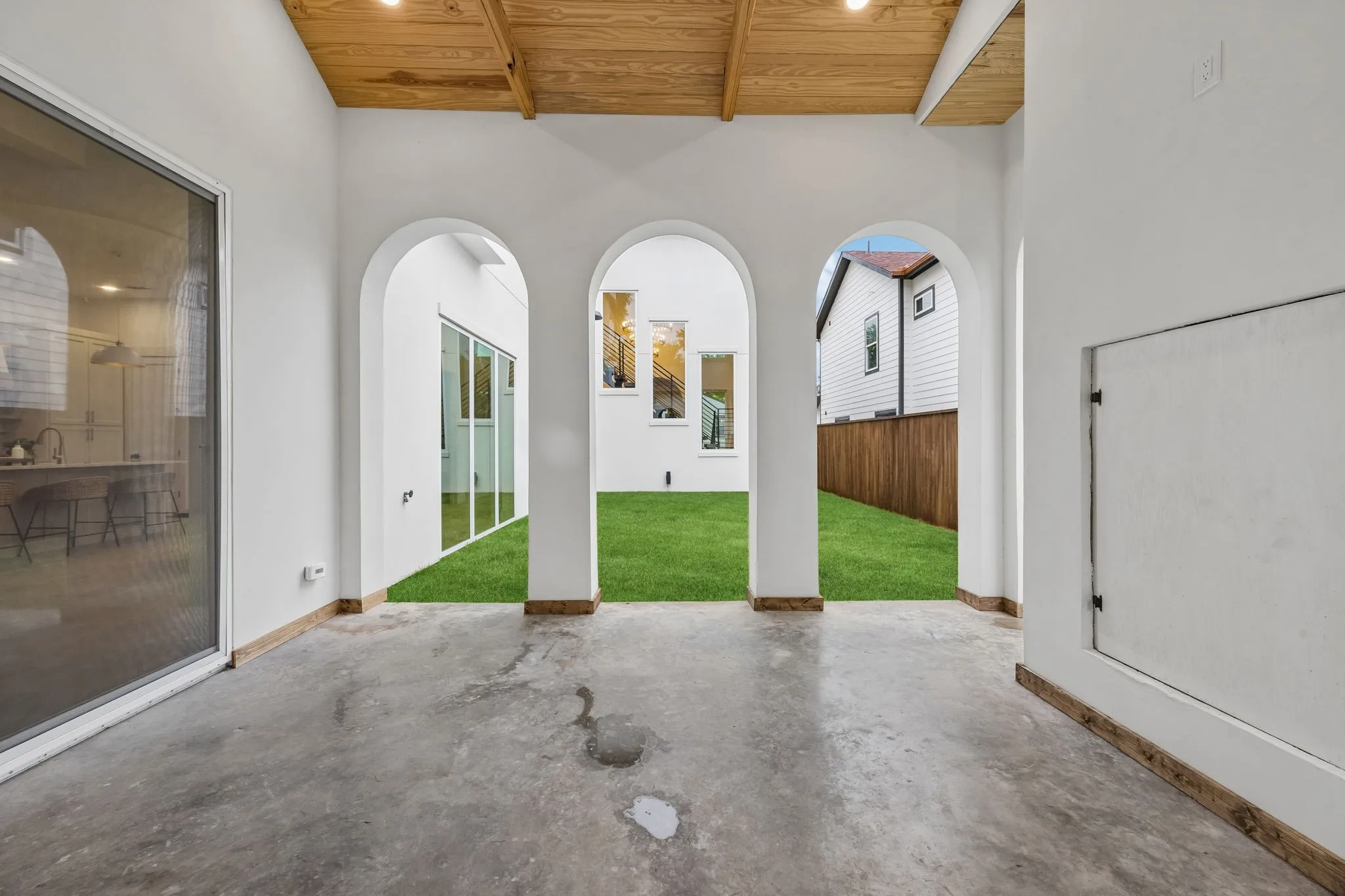 Covered patio featuring a wood-finish ceiling with recessed lighting and three arched openings leading to the yard