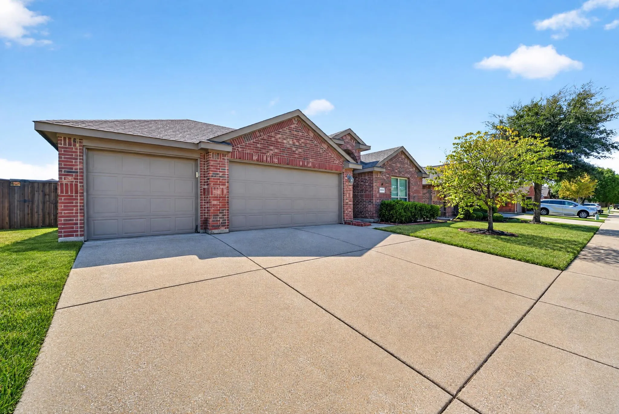 Brick exterior with a three-car garage, concrete driveway, and front lawn landscaping