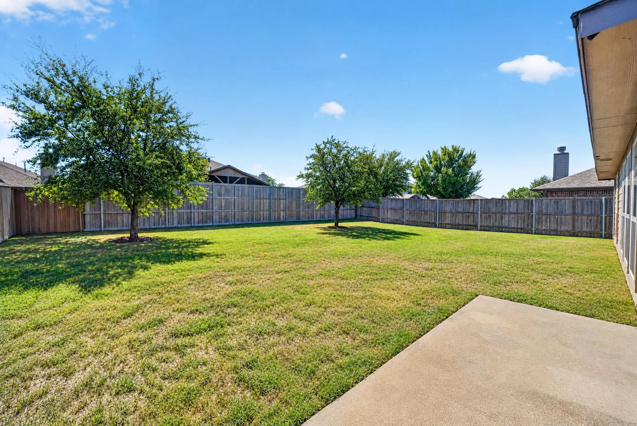 Expansive backyard featuring a privacy fence, two mature trees, and a concrete patio