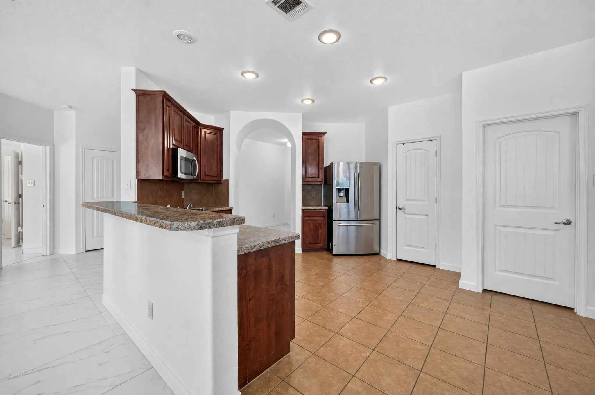 Kitchen featuring wood-finish cabinetry, stainless steel appliances, a breakfast bar with stone-look countertop, recessed lighting, and tile flooring