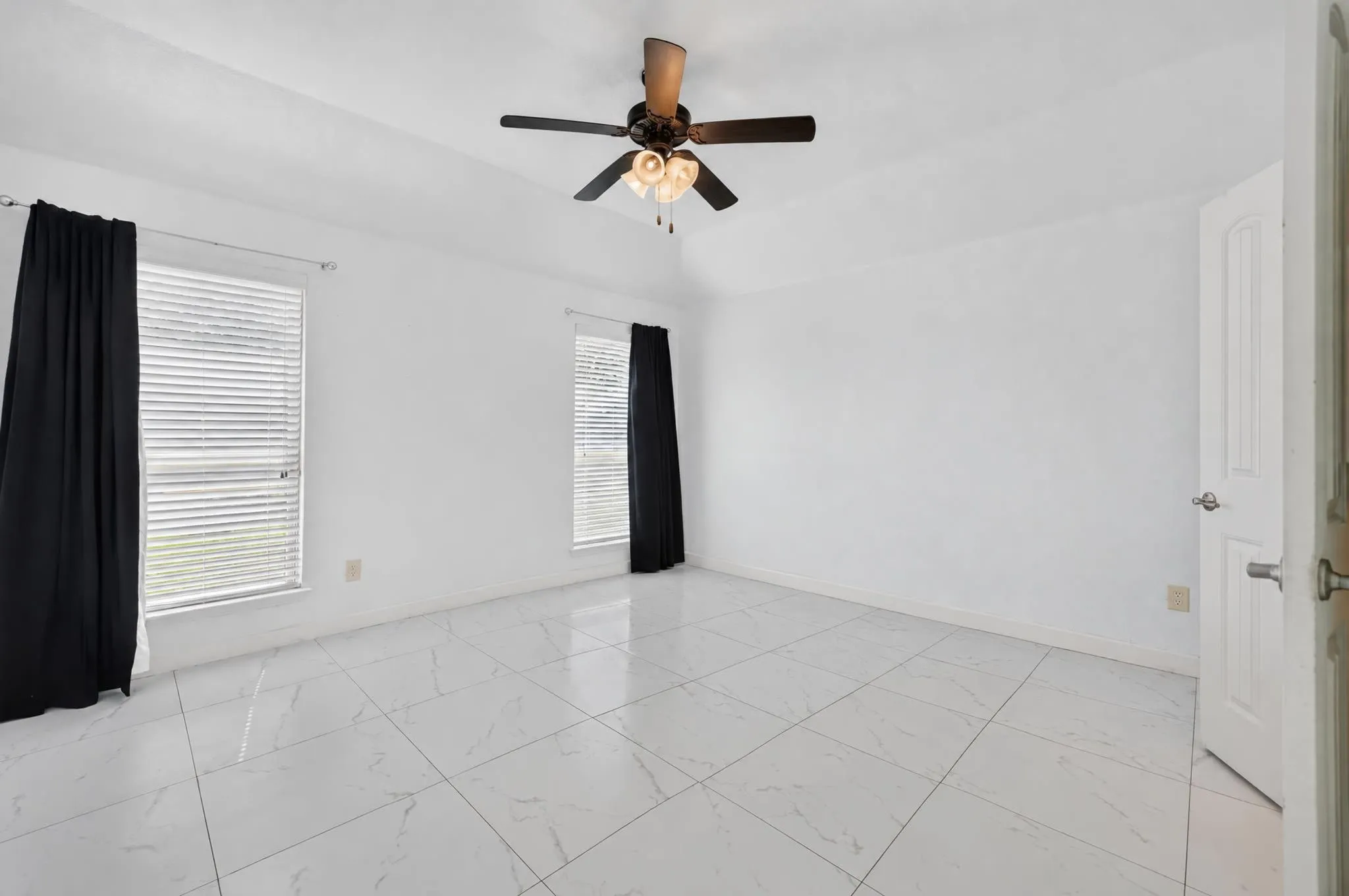 Vaulted ceiling with a ceiling fan, two windows with blinds, and white tile flooring