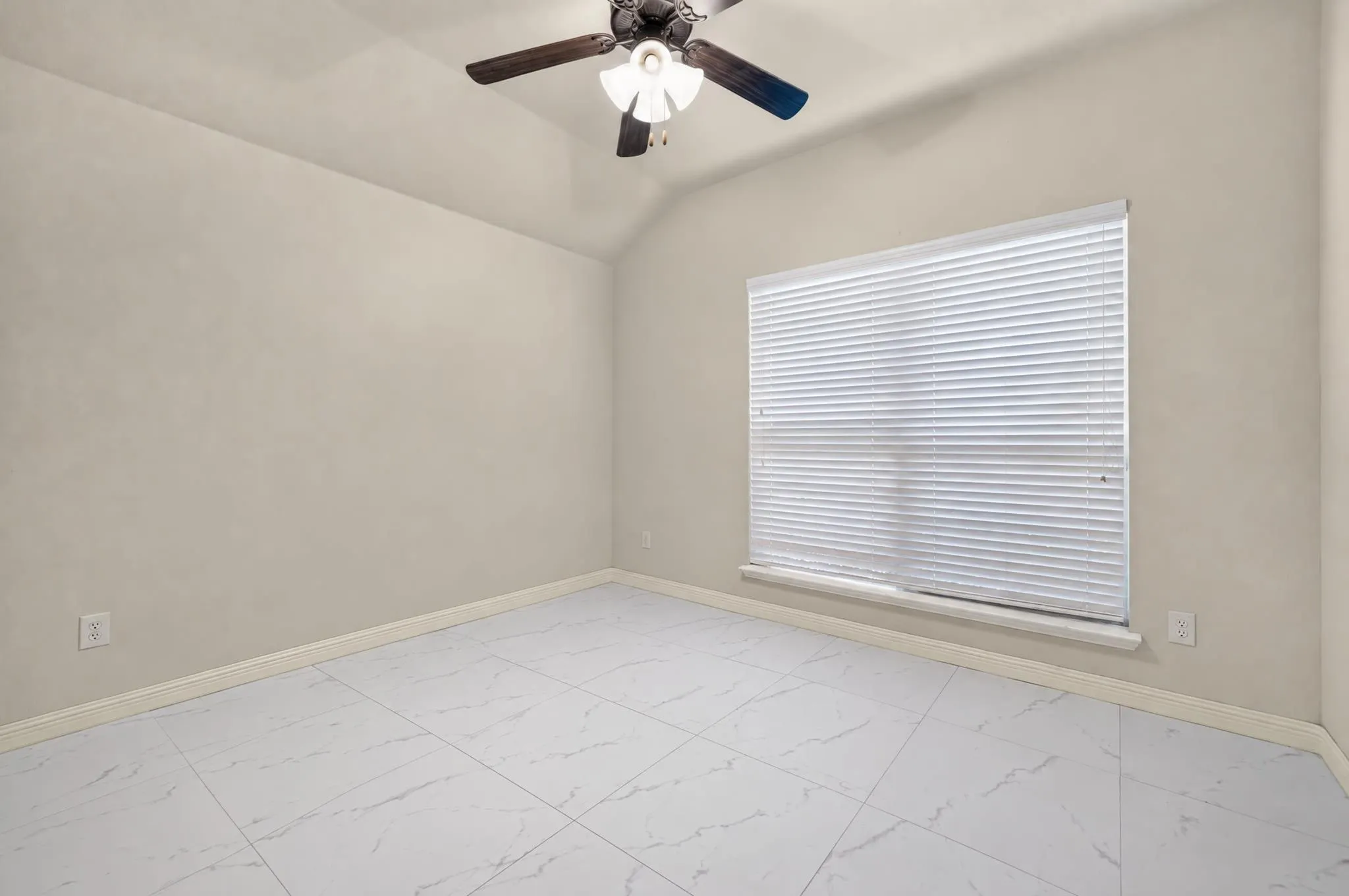 Vaulted ceiling, ceiling fan, large window with blinds, tile flooring, and light-toned walls