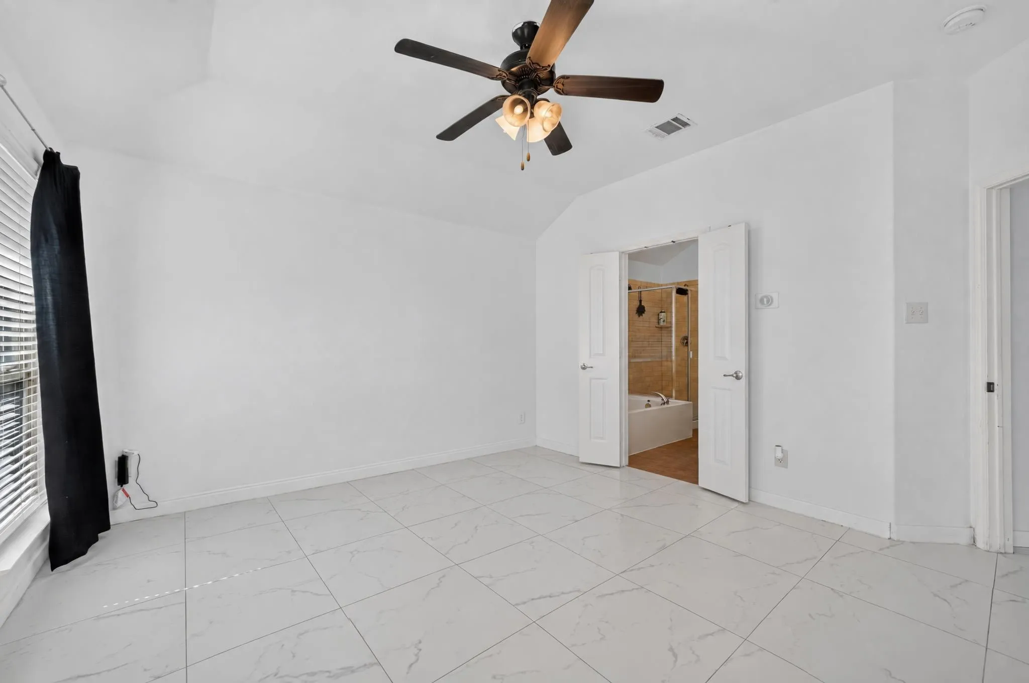 Vaulted ceiling with a ceiling fan, white tile flooring, and double doors opening to a bathroom with a soaking tub and shower