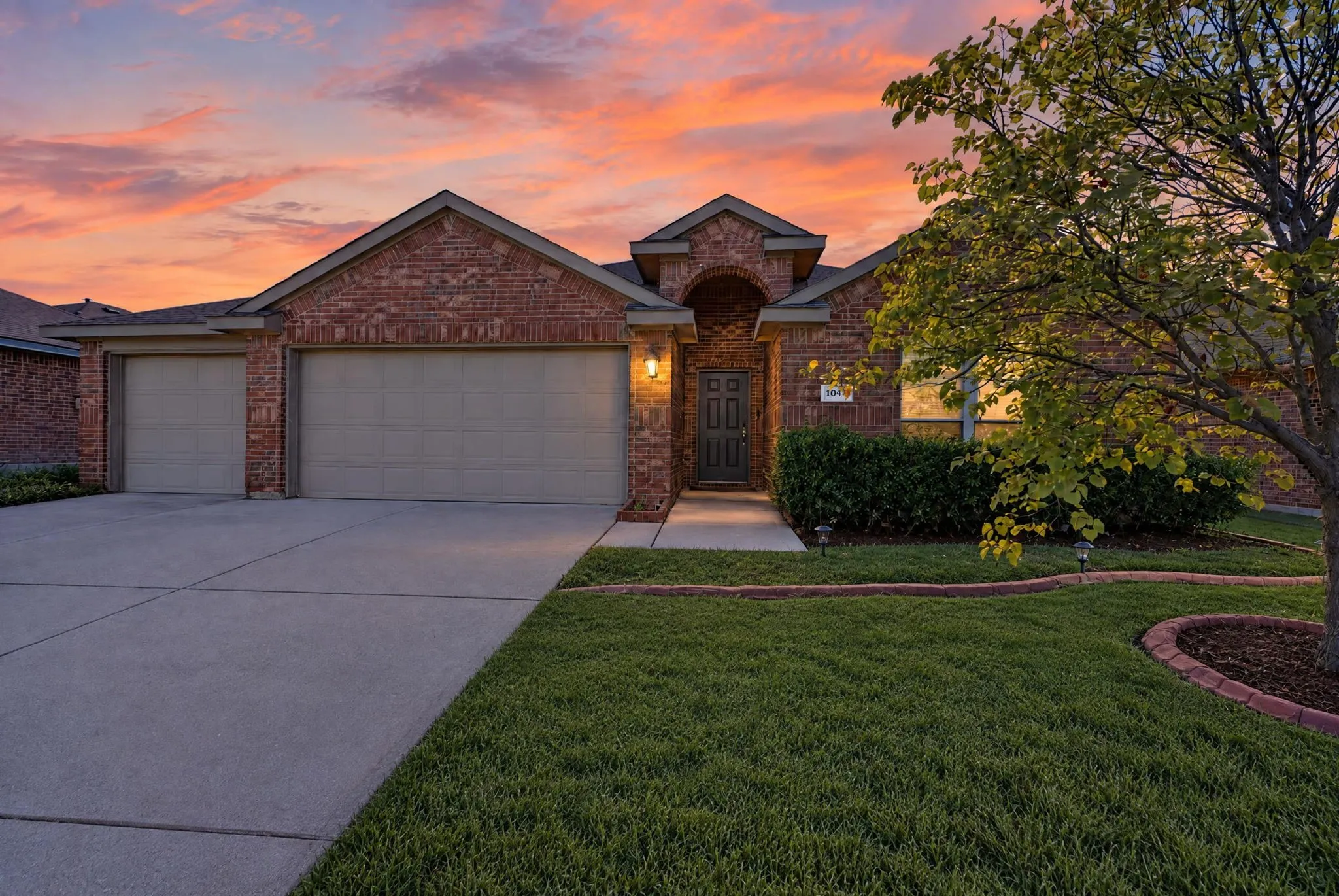 Brick exterior with a gabled roofline, two-car garage with panel doors, concrete driveway, and established front landscaping