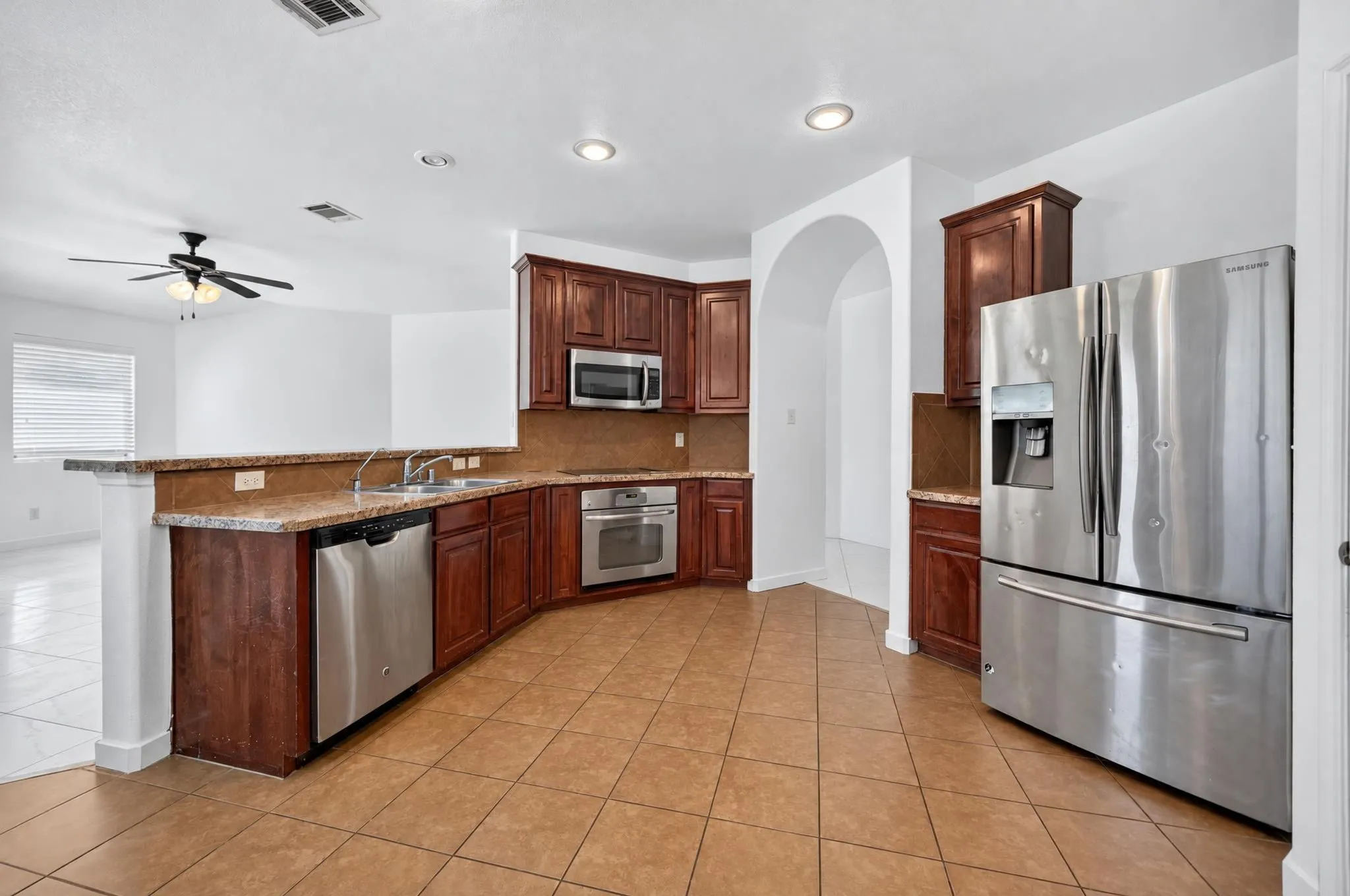 Kitchen featuring stainless steel appliances, wood-finish cabinetry, tile flooring, recessed lighting, and an arched doorway