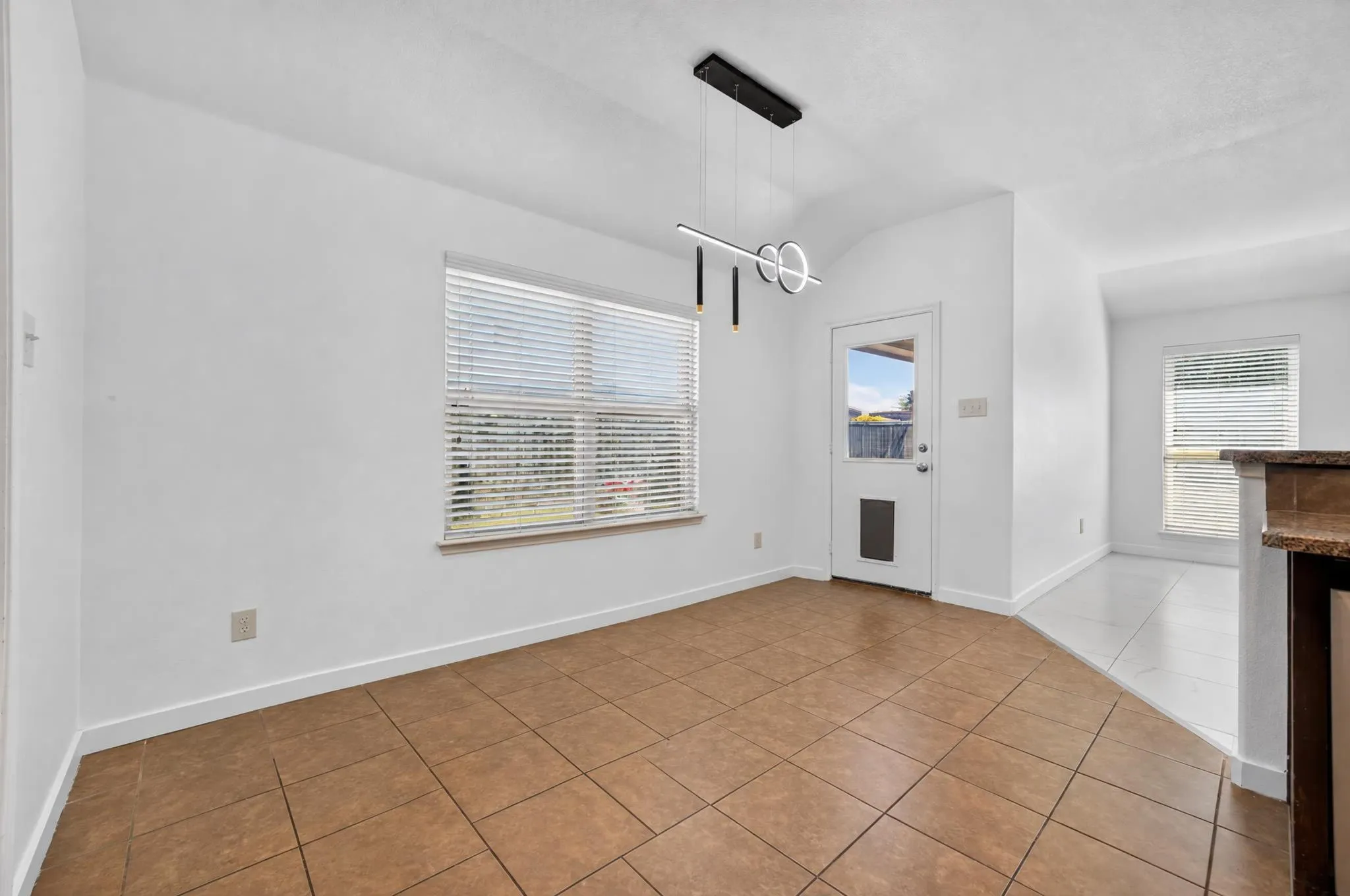 Tile flooring in a neutral tone, modern linear pendant light fixture, a window with blinds, and a door providing exterior access