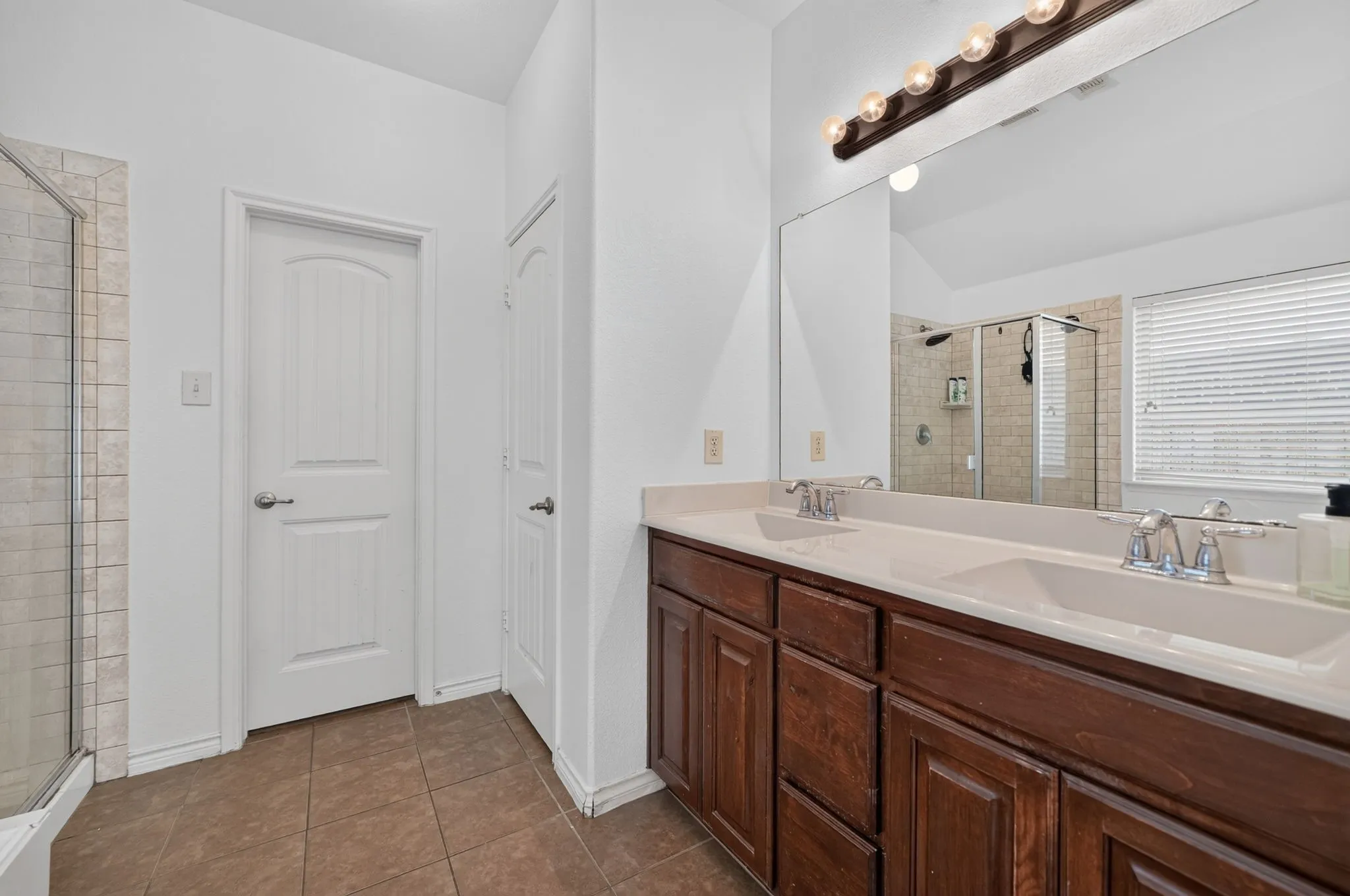 Double vanity with integrated sinks, wood-finish cabinetry, and a large wall-mounted mirror