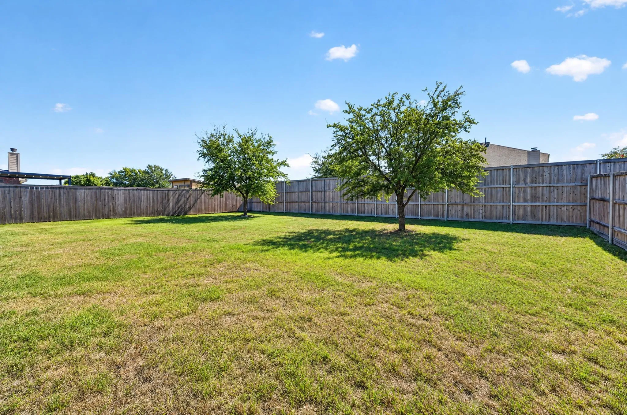 Expansive backyard featuring a natural grass lawn, full privacy fencing, and mature trees providing natural shade
