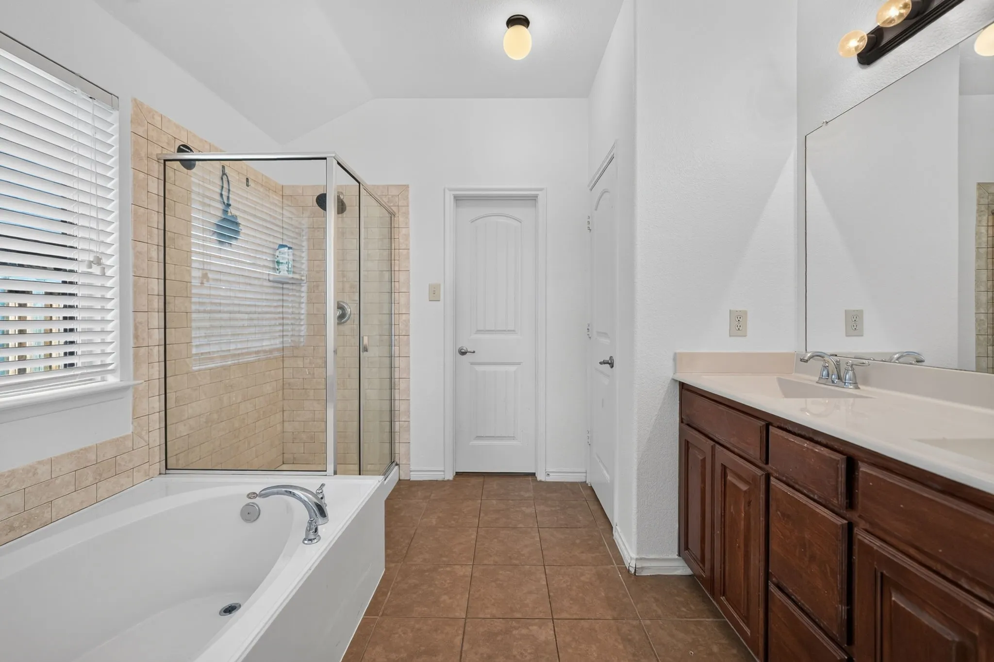 Enclosed glass shower with tiled surround, soaking tub, dual vanity with wood-finish cabinetry, and tiled flooring
