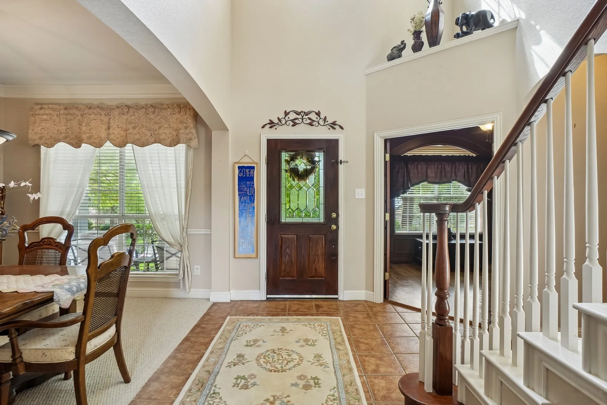Two-story foyer with tile flooring, a dark wood front door with decorative glass, and a prominent staircase with white balusters and a wood handrail