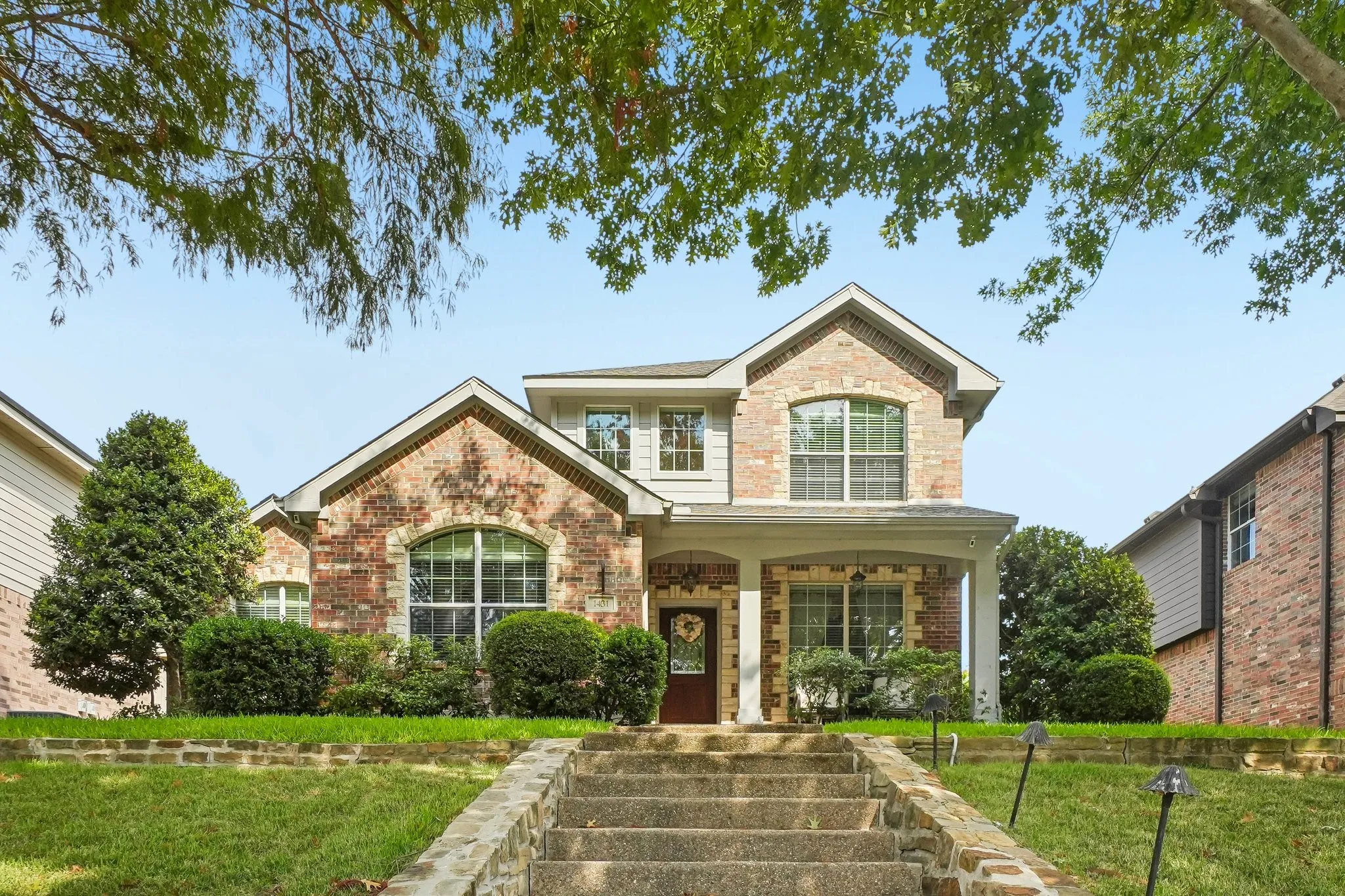 Welcoming two-story brick residence featuring a peaked gable roofline, arched transom windows, and a columned front porch with stone entry steps