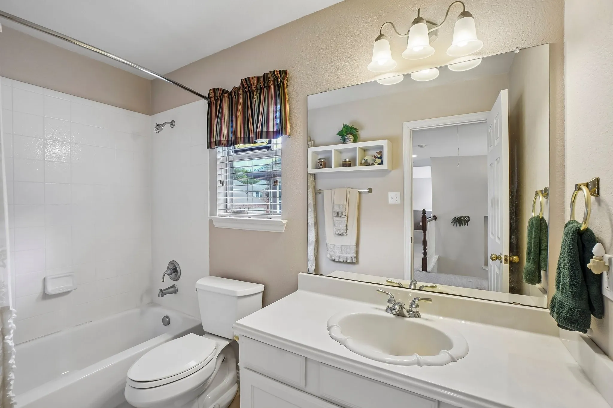 White tiled shower-tub combination, single-sink vanity with white countertop, chrome fixtures, and a wall-mounted mirror with integrated lighting