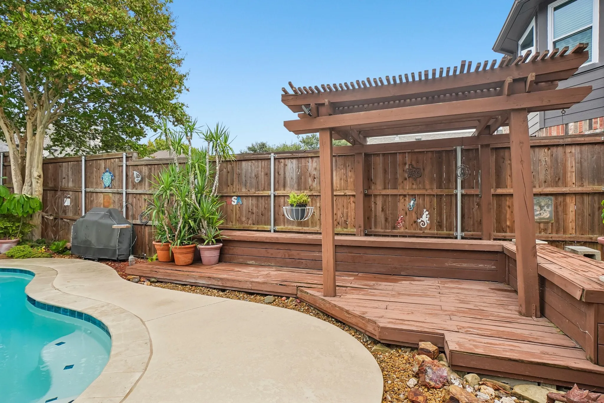 Curved-edge swimming pool with concrete decking, a wood privacy fence, and a wooden pergola with an integrated bench seating area