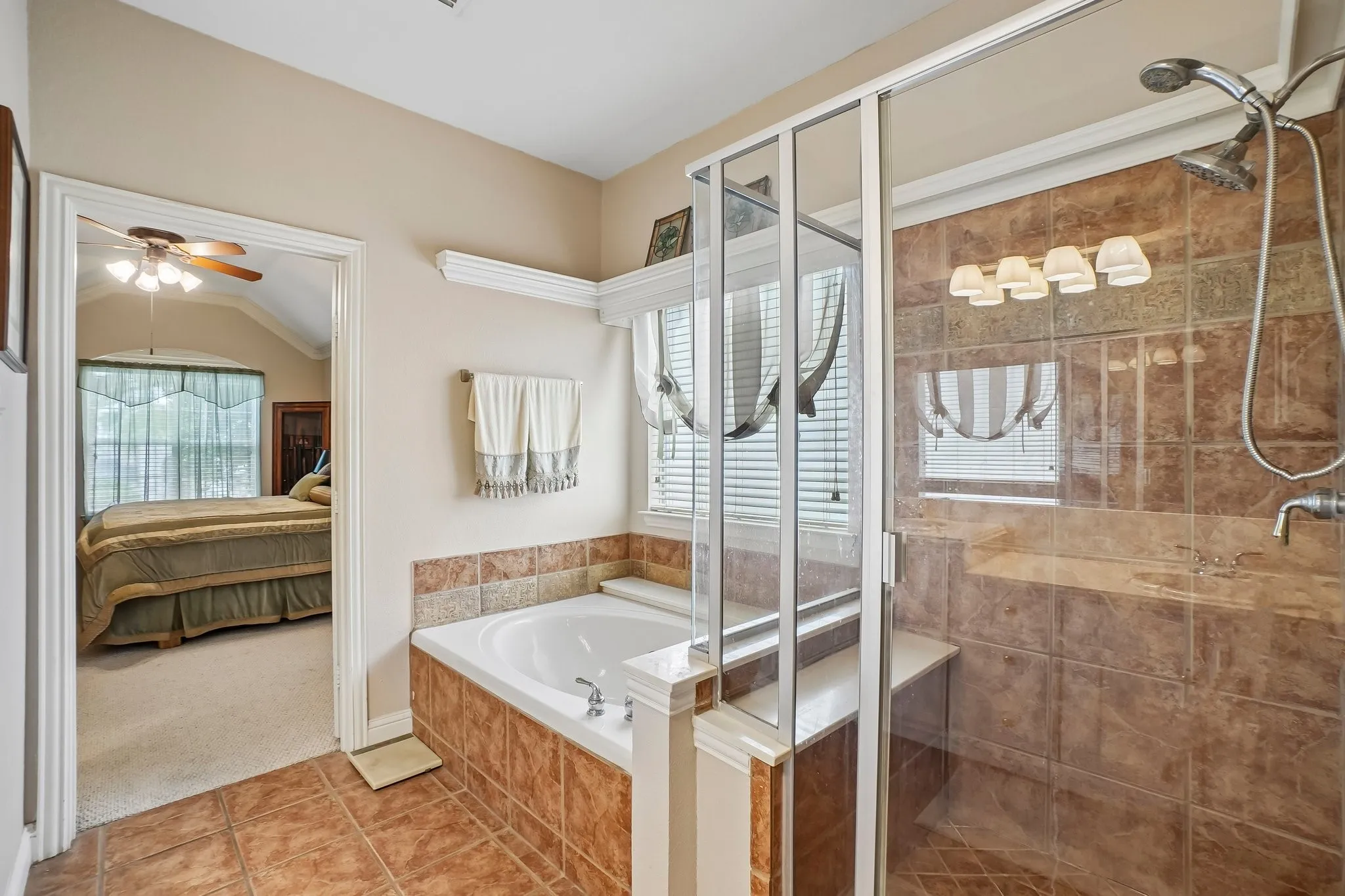 Tiled flooring leading to a built-in bathtub with tiled surround, a separate glass-enclosed shower with tiled walls and a built-in bench, and a window with blinds