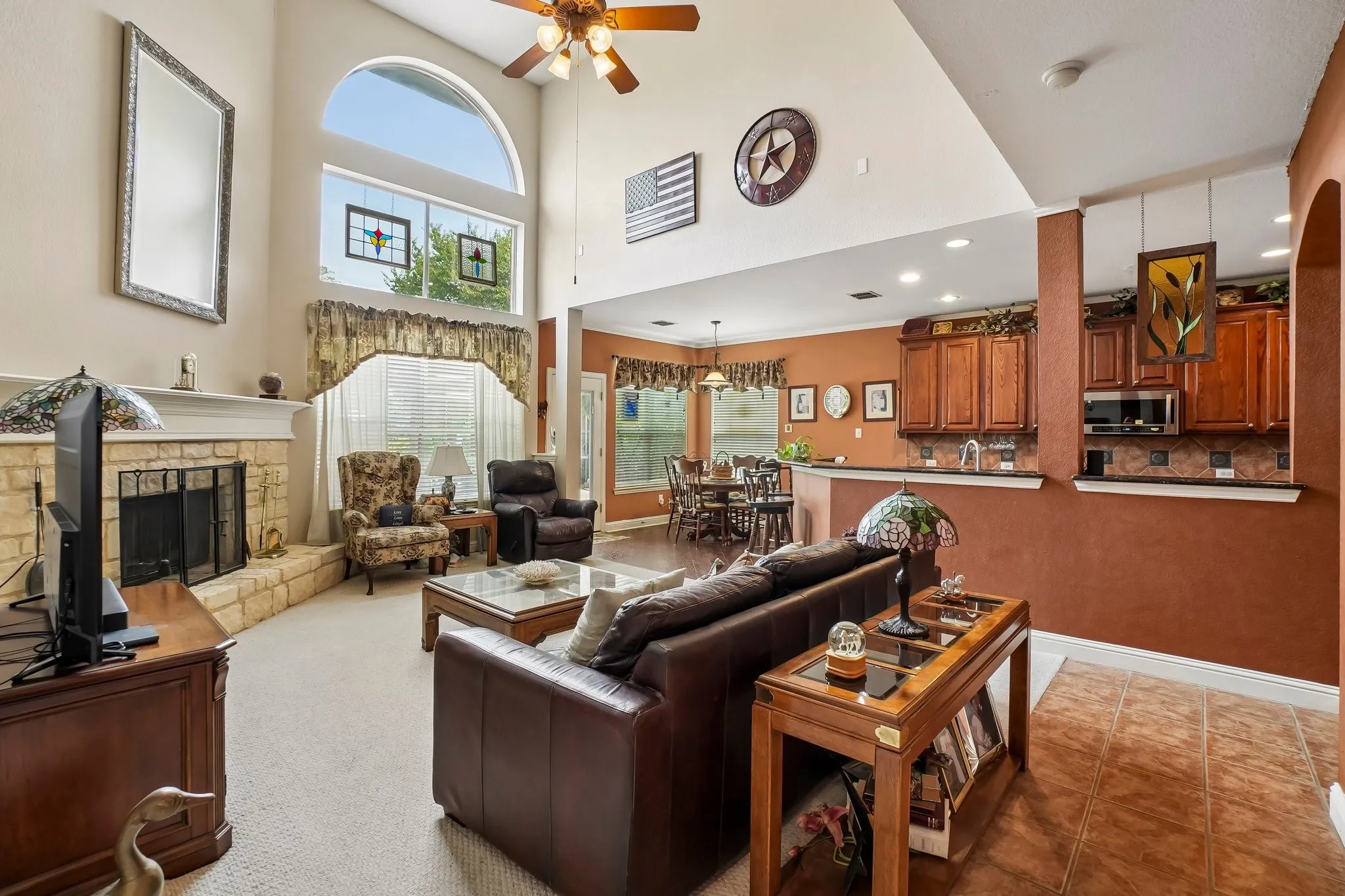 Vaulted ceilings with an arched window, stone-clad fireplace, and wood-finish kitchen cabinetry