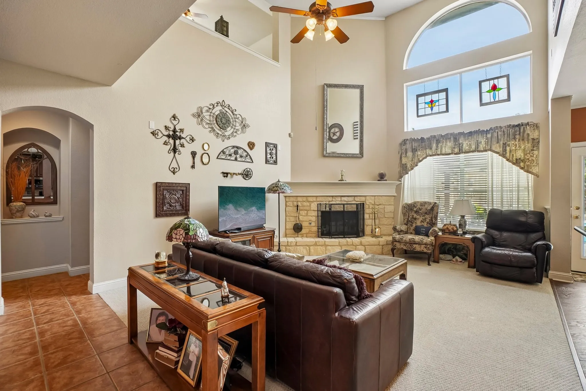 Vaulted ceiling with an arched window, stone-faced fireplace, and an upper architectural shelf