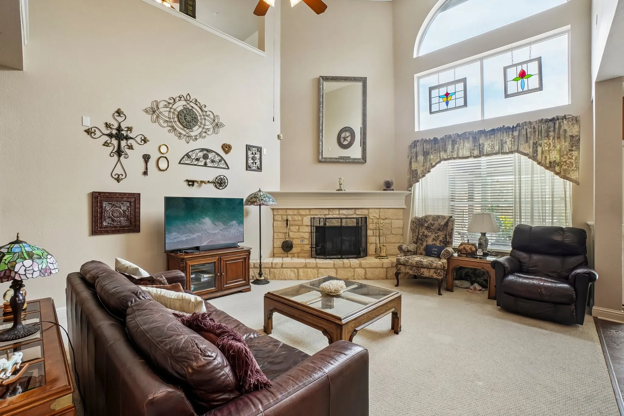 Two-story living area featuring a stone-clad fireplace, high vaulted ceilings, and an arched window with transom panels