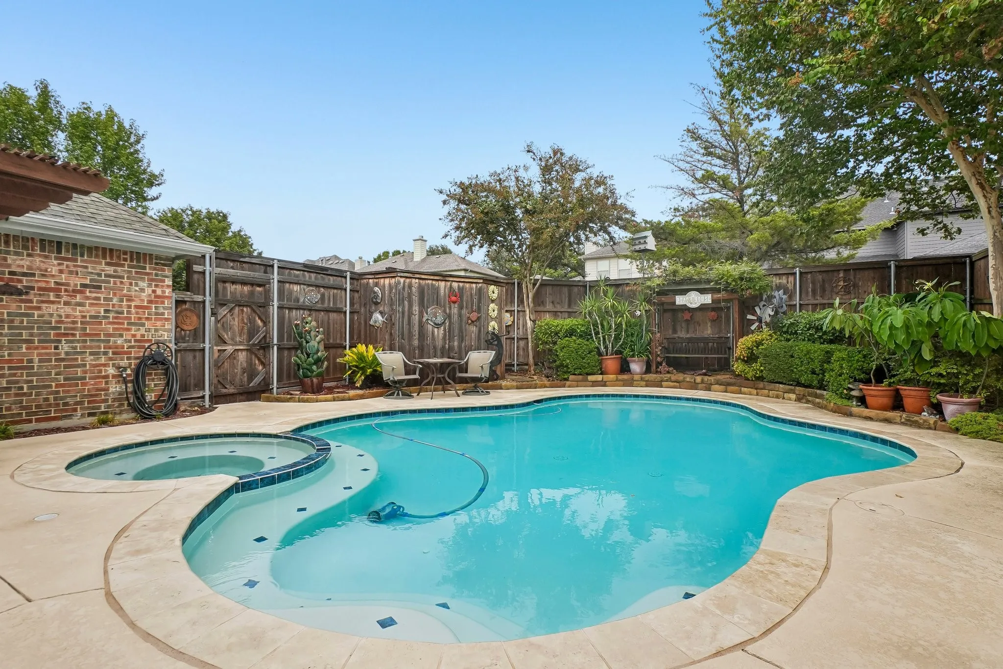 Freeform swimming pool with an integrated spa, expansive concrete decking, and perimeter privacy fencing