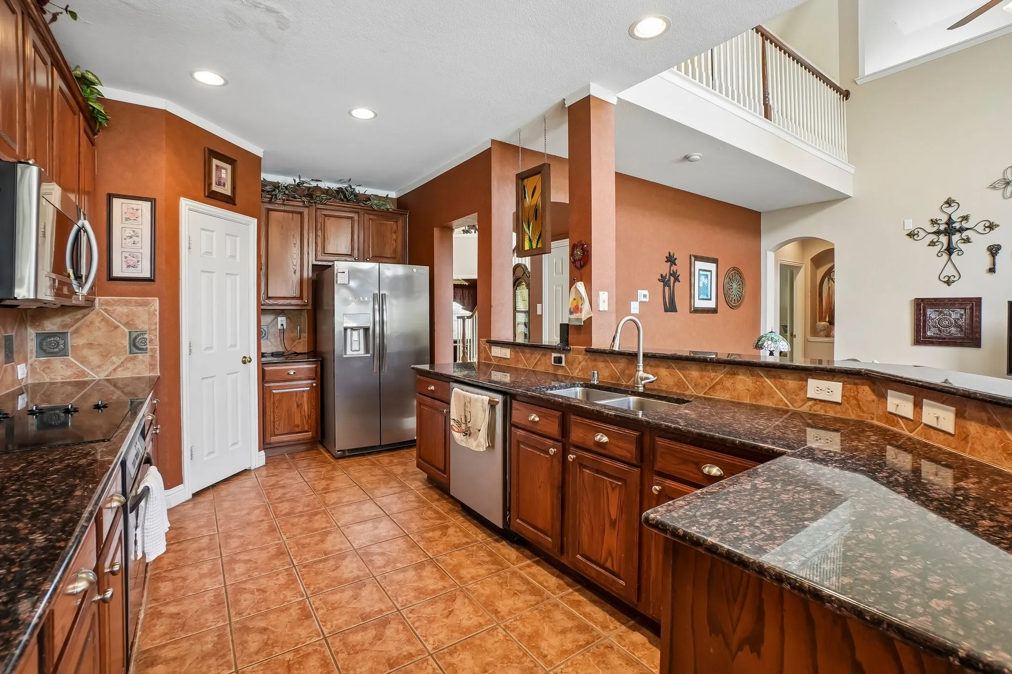 Spacious kitchen featuring rich wood cabinetry, granite countertops, stainless steel appliances, and terracotta tile flooring