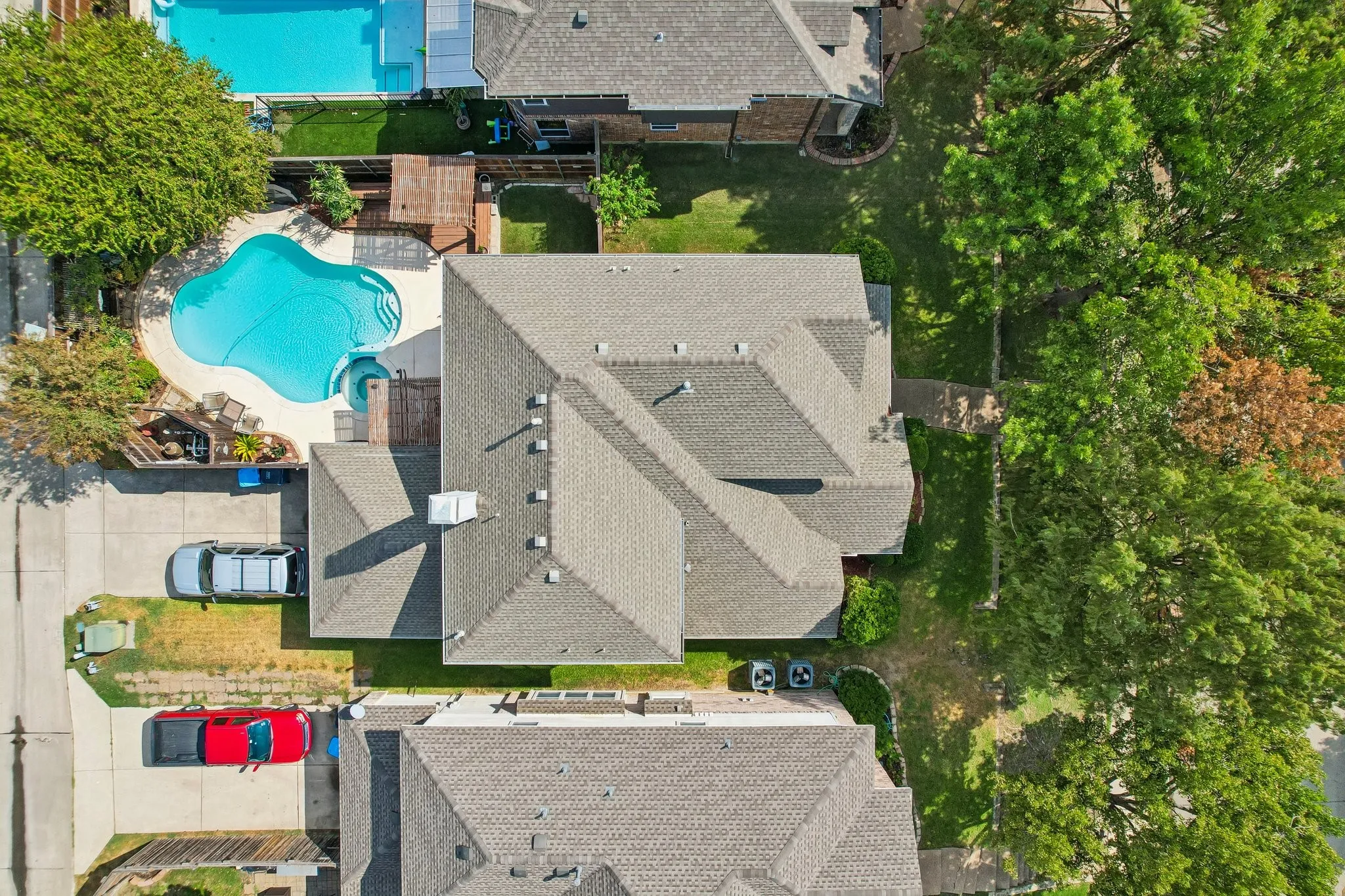 Freeform swimming pool with integrated spa, concrete decking, and adjacent wood-finish deck