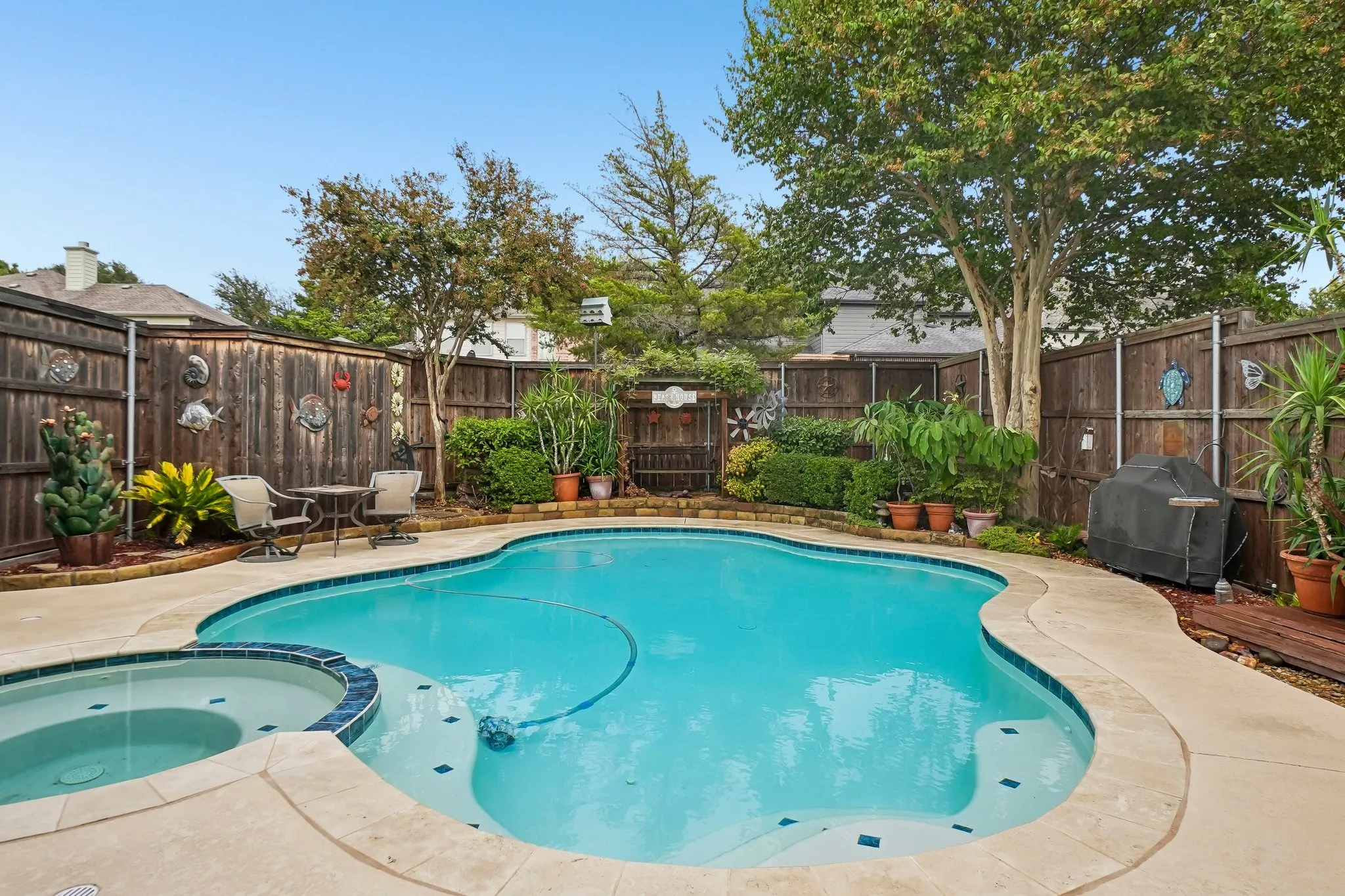Freeform pool with an integrated spa, surrounded by a concrete patio, and a privacy fence