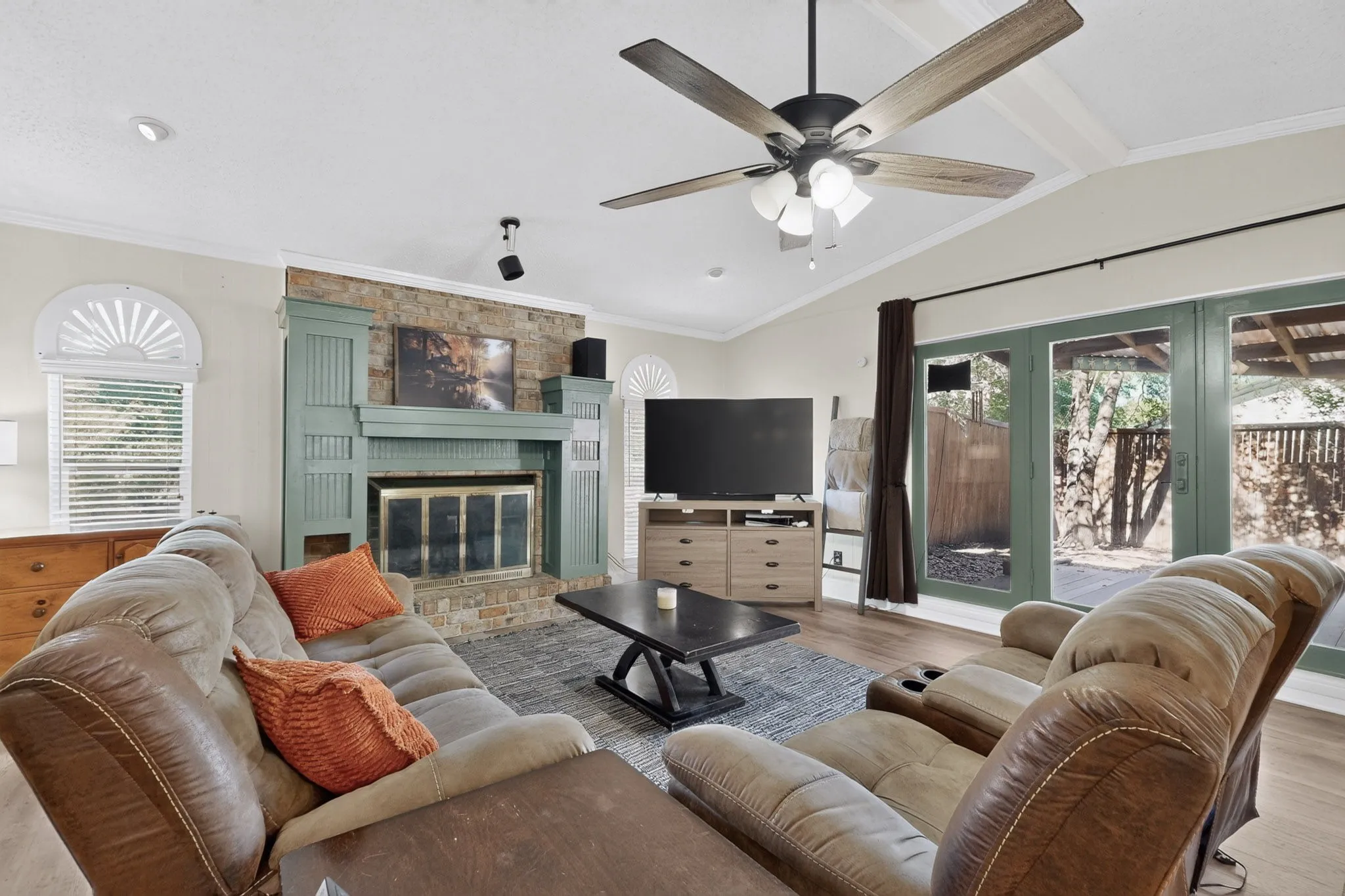 Vaulted ceilings, wood-finish flooring, stone-faced fireplace with a decorative mantel, ceiling fan, and sliding glass doors