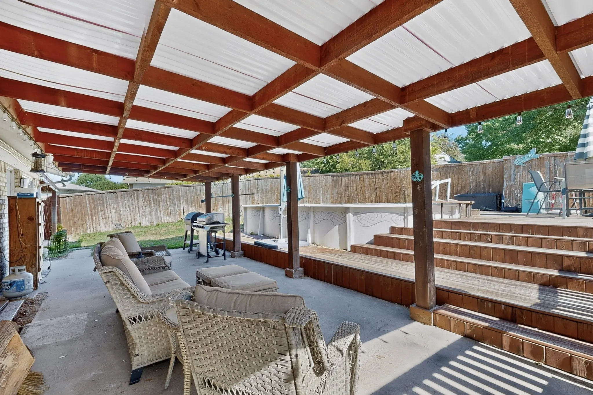 Covered concrete patio with an adjacent multi-level wood deck, supported by substantial wood columns and featuring a privacy fence